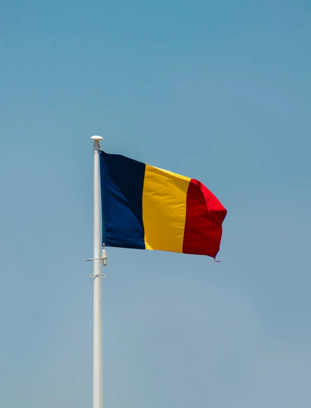 Steagul României, tricolor albastru-galben-roșu, fluturând pe un catarg sub un cer senin.