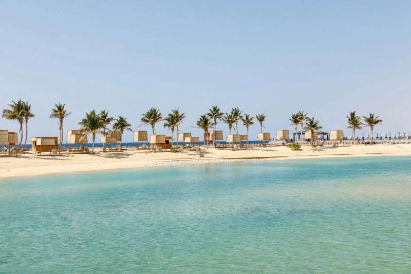 Plajă liniștită în Hurghada, Egipt, cu apă turcoaz, palmieri și foișoare de lemn.