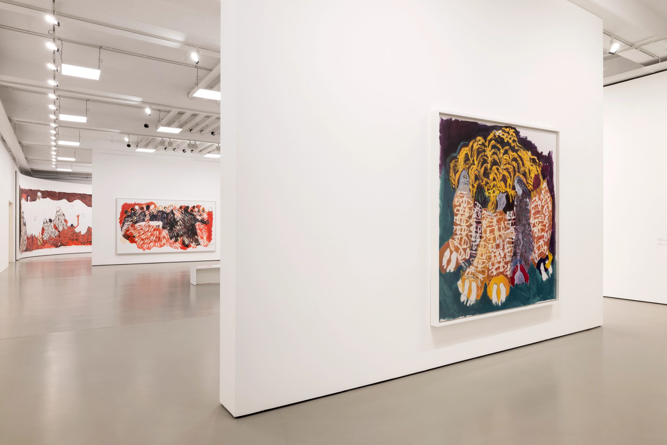 A brightly lit modern art gallery with white walls displays several large abstract paintings, including a prominent colorful piece in the foreground with yellow, orange, and purple hues.