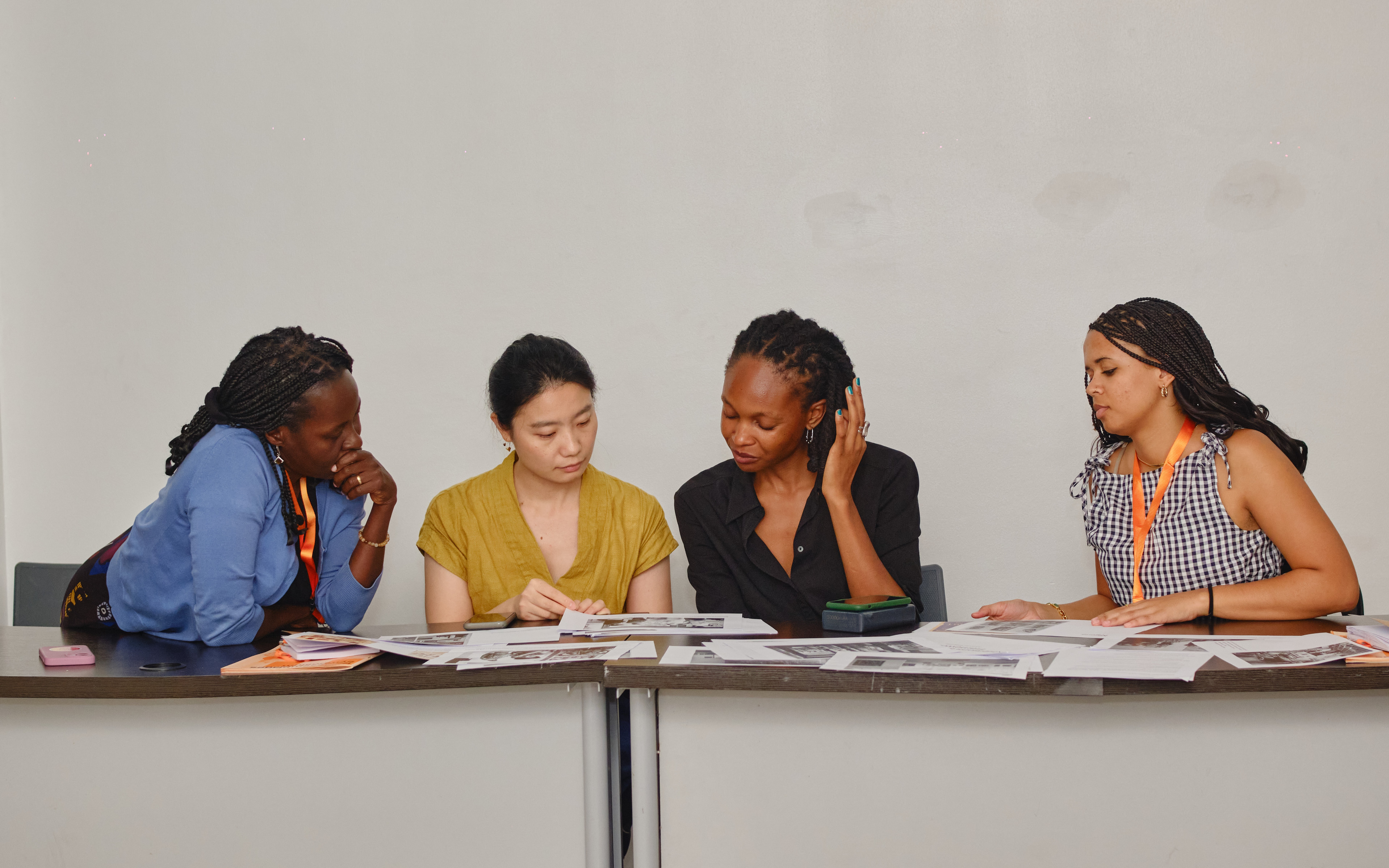 Four women sit at a table, reviewing documents spread before them.