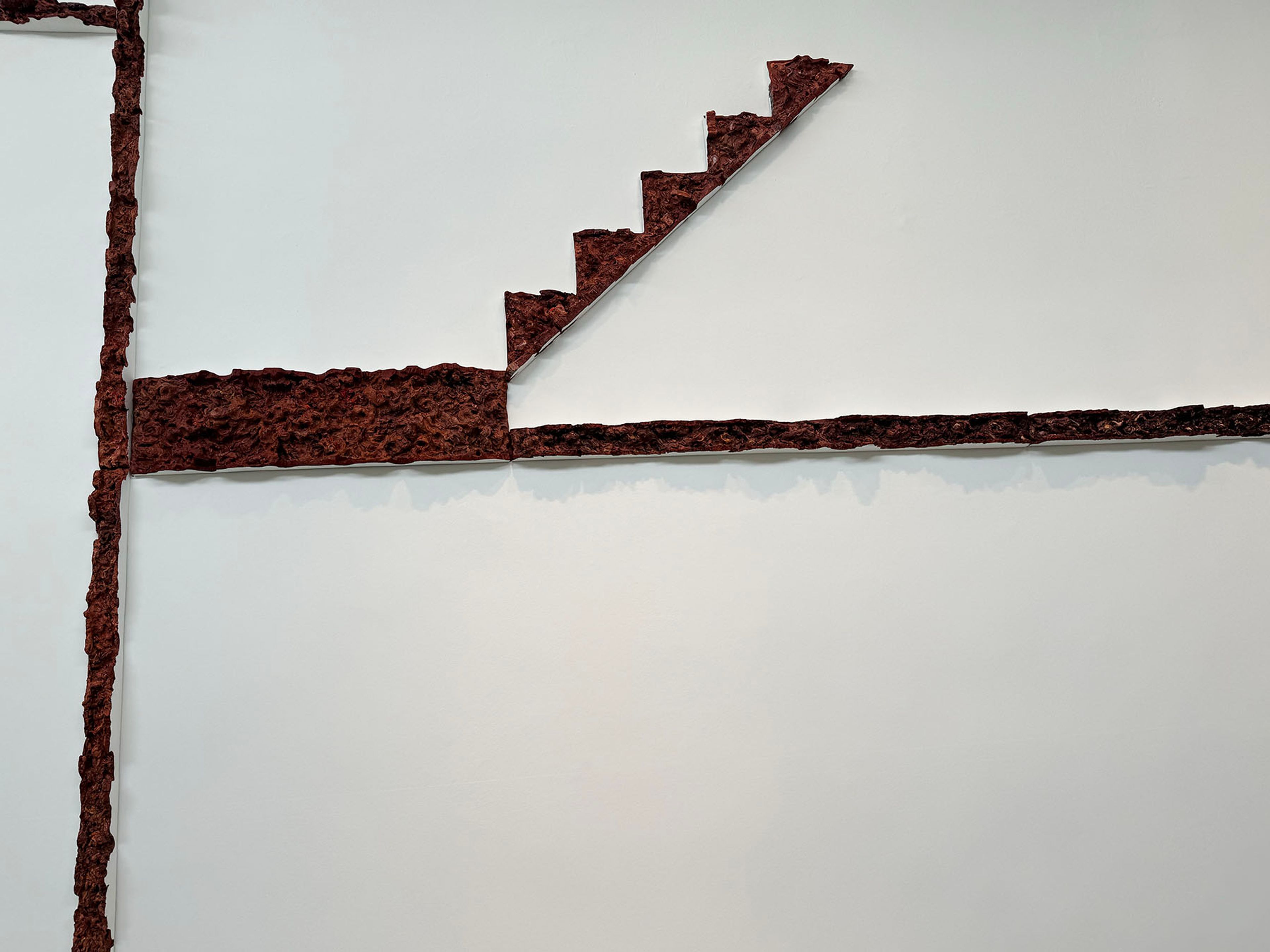 Rough, reddish-brown lines form an abstract vertical, horizontal, and stepped diagonal pattern on a white background.