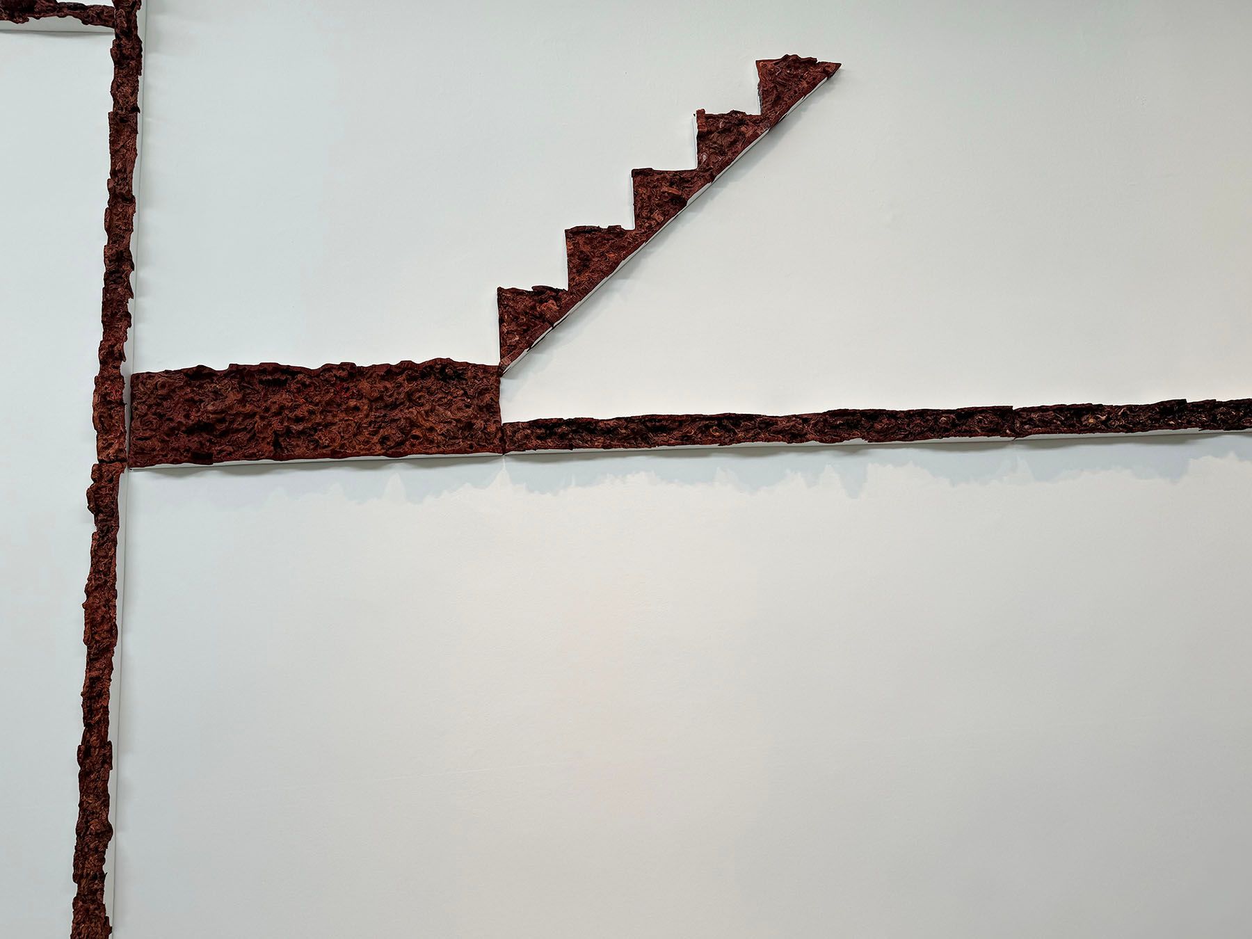 Rough, reddish-brown lines form an abstract vertical, horizontal, and stepped diagonal pattern on a white background.