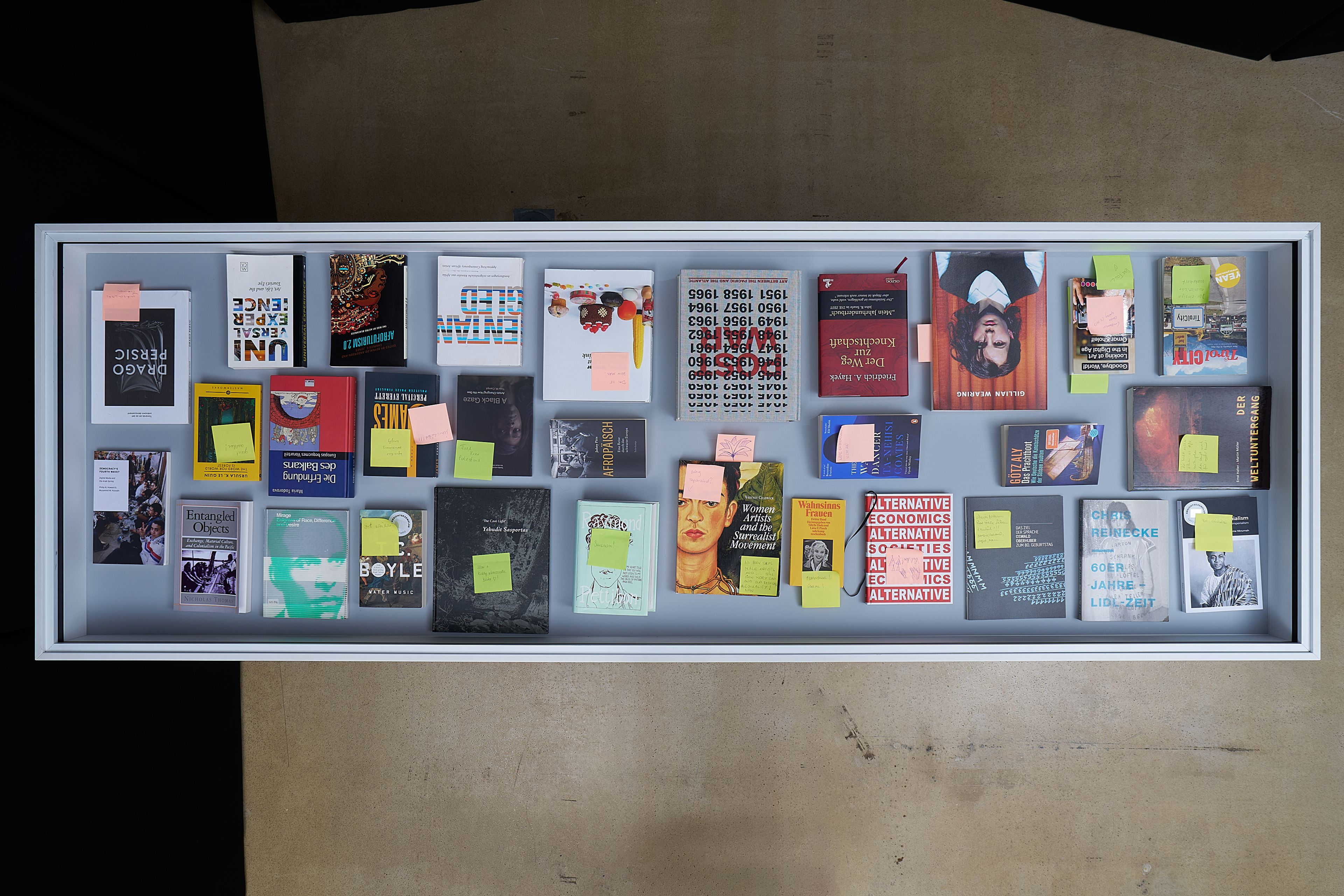 Overhead view of a display case filled with various books and printed materials, many marked with sticky notes.