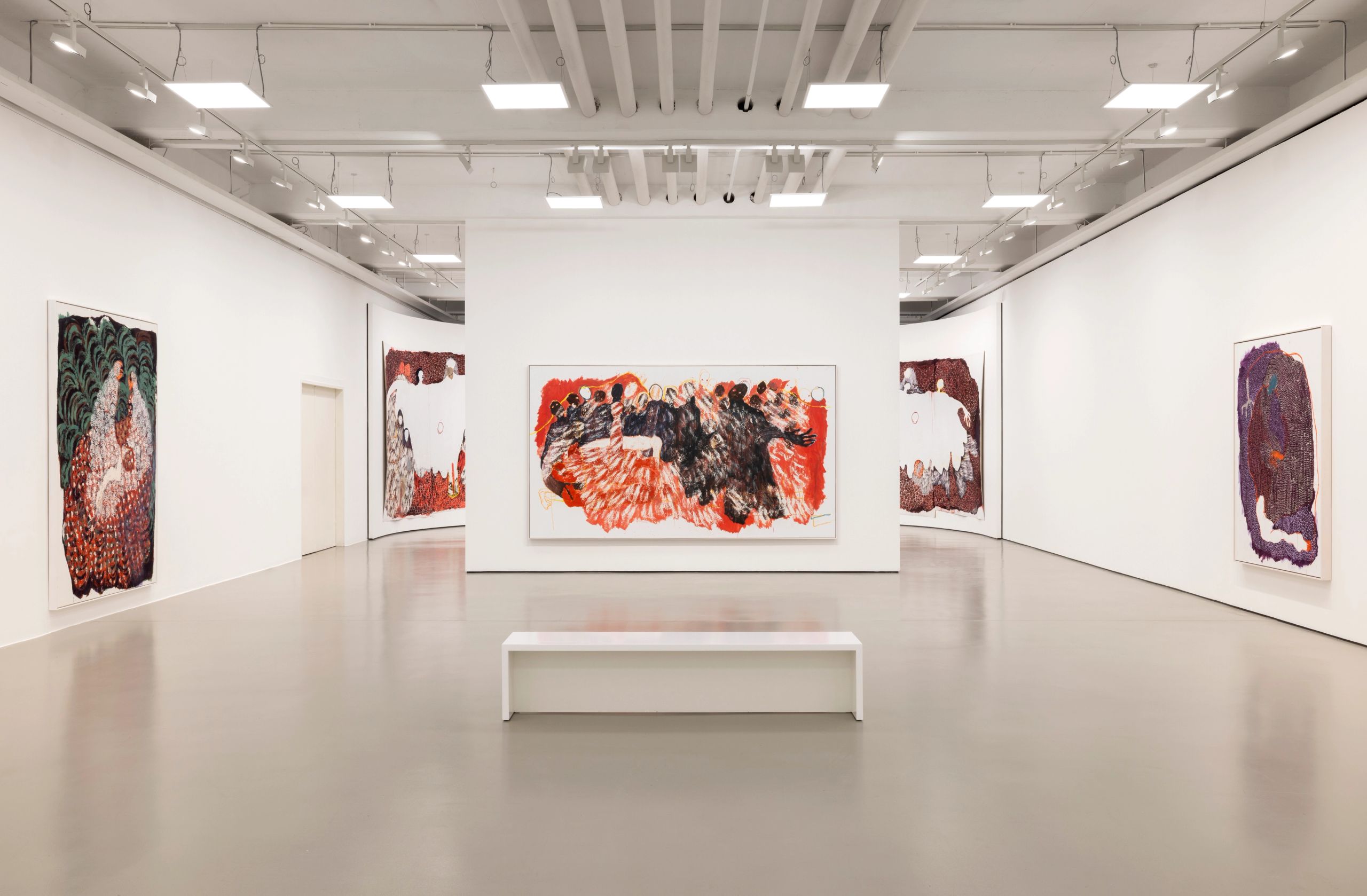 A modern art gallery with abstract paintings on white walls and a white bench.