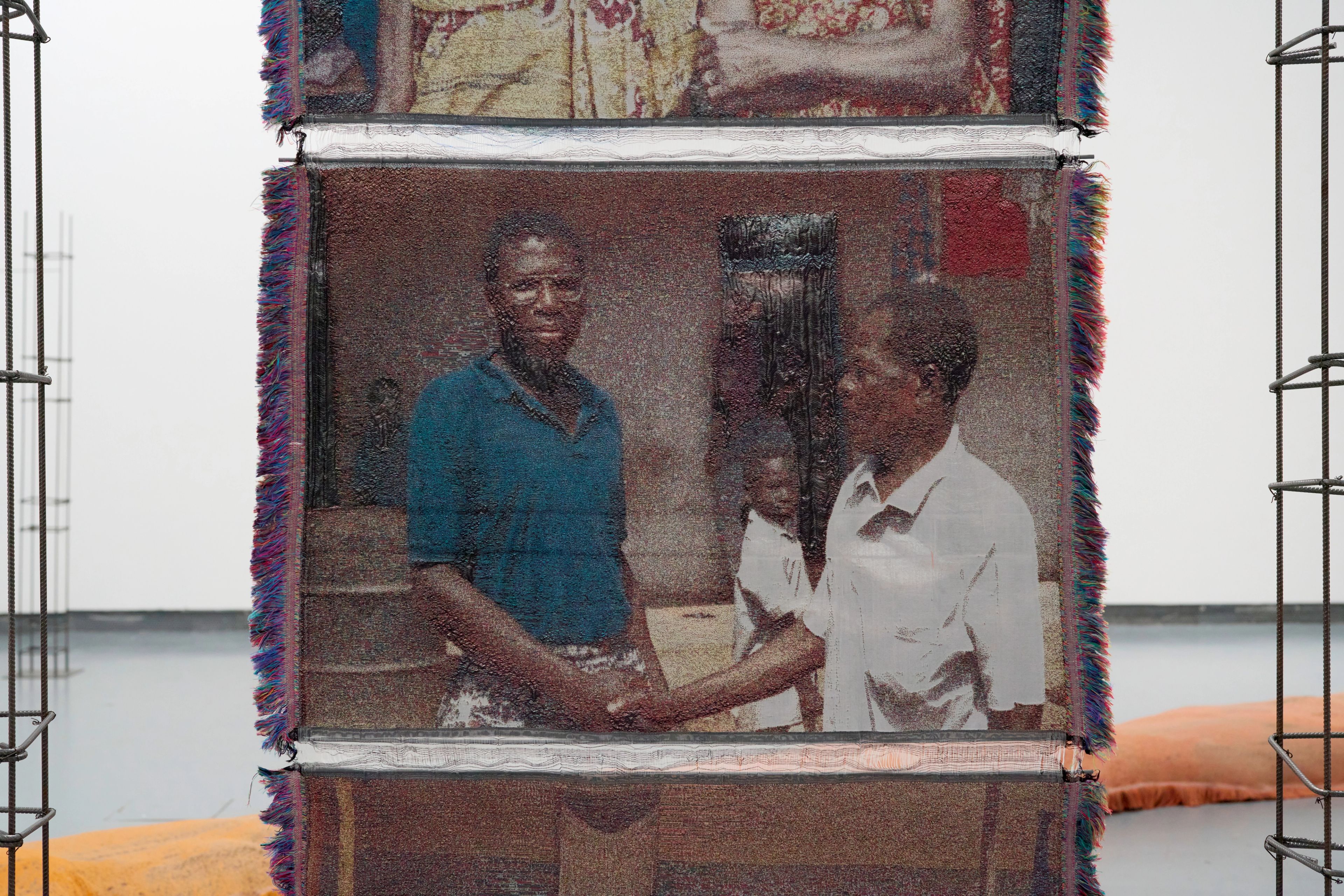 A woven textile panel showing a textured image of two Black men shaking hands, with a child in the background.