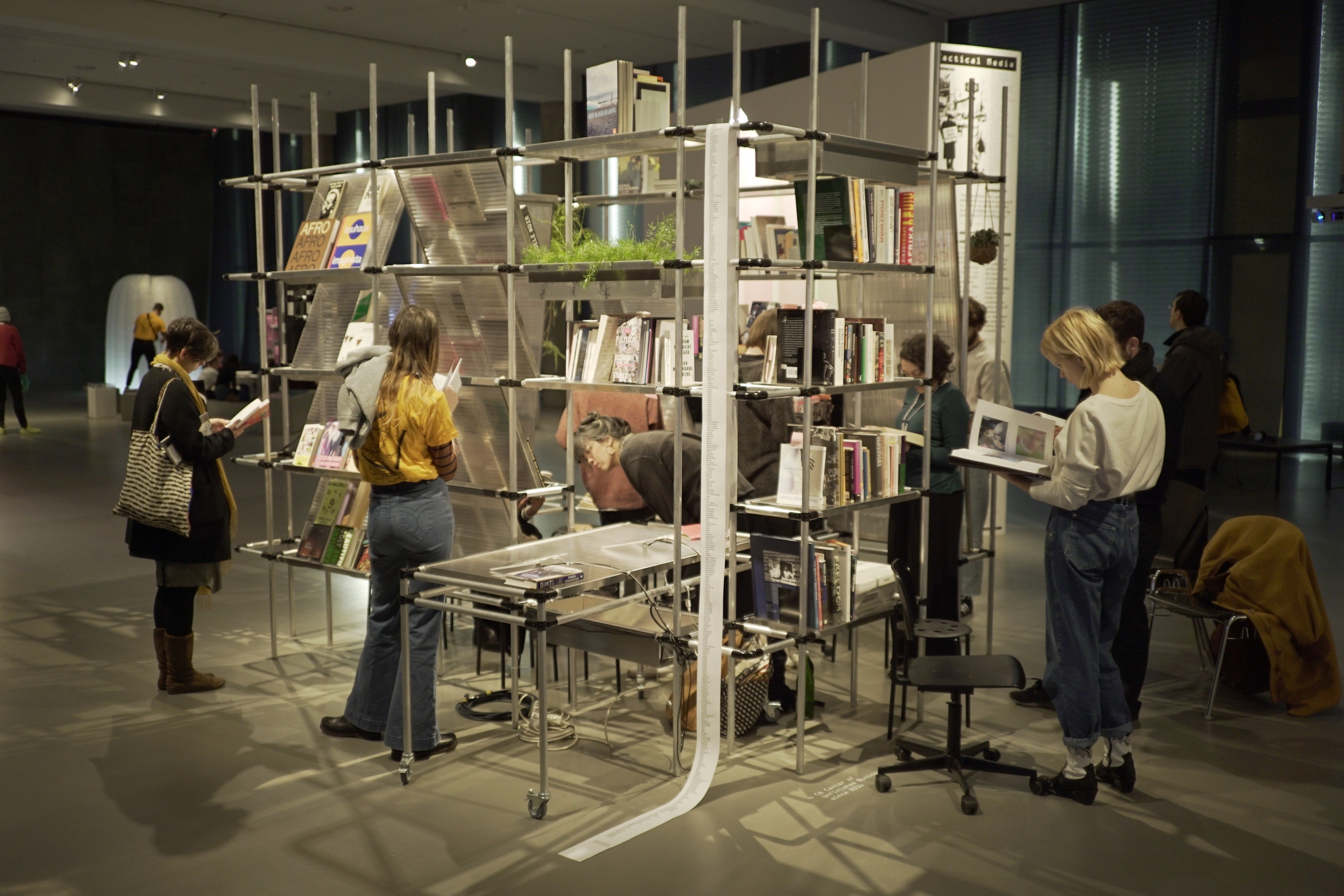 An innovative, multi-level book display with several people browsing its contents in a modern gallery.