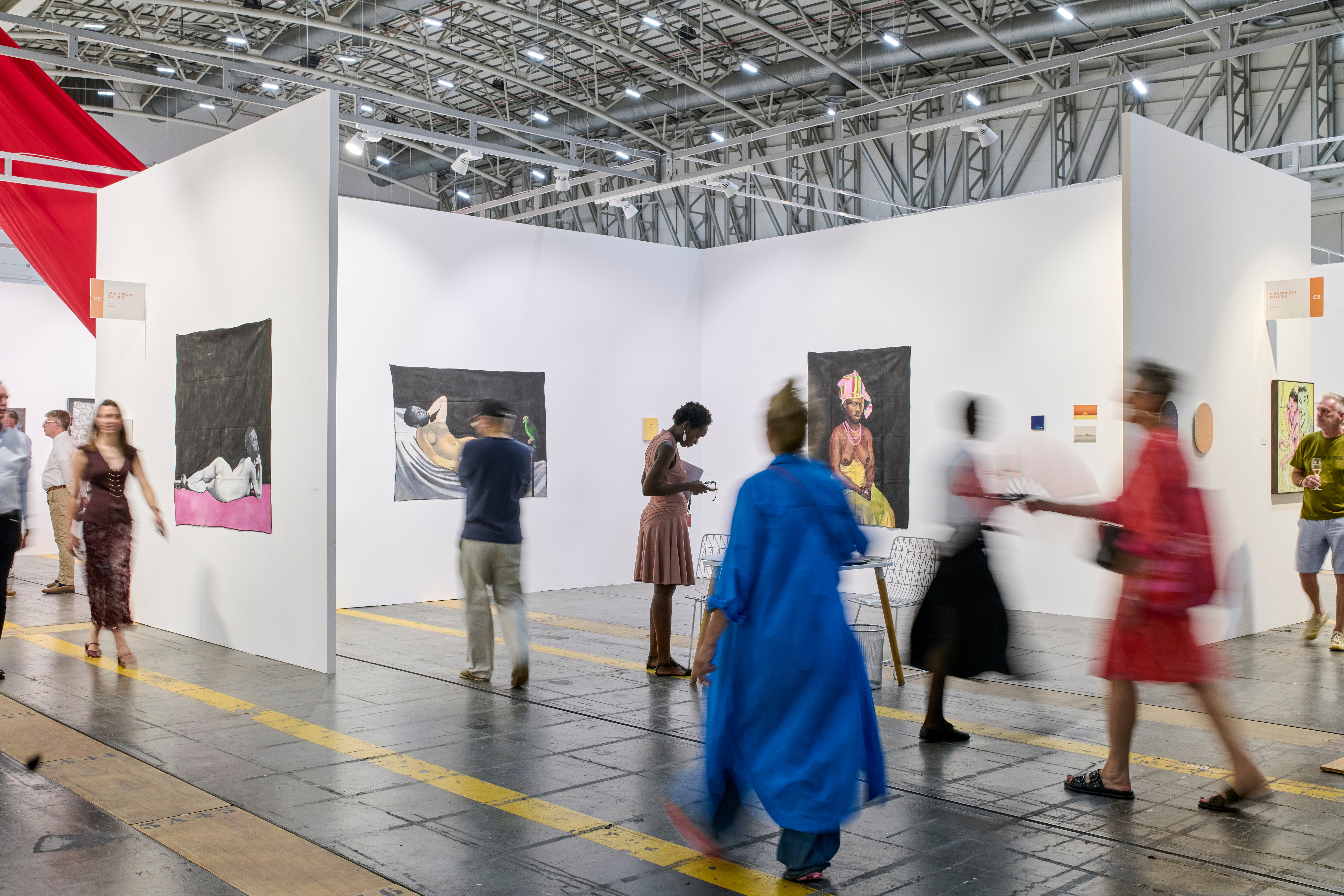 Visitors view paintings displayed on white walls in a large art exhibition hall.