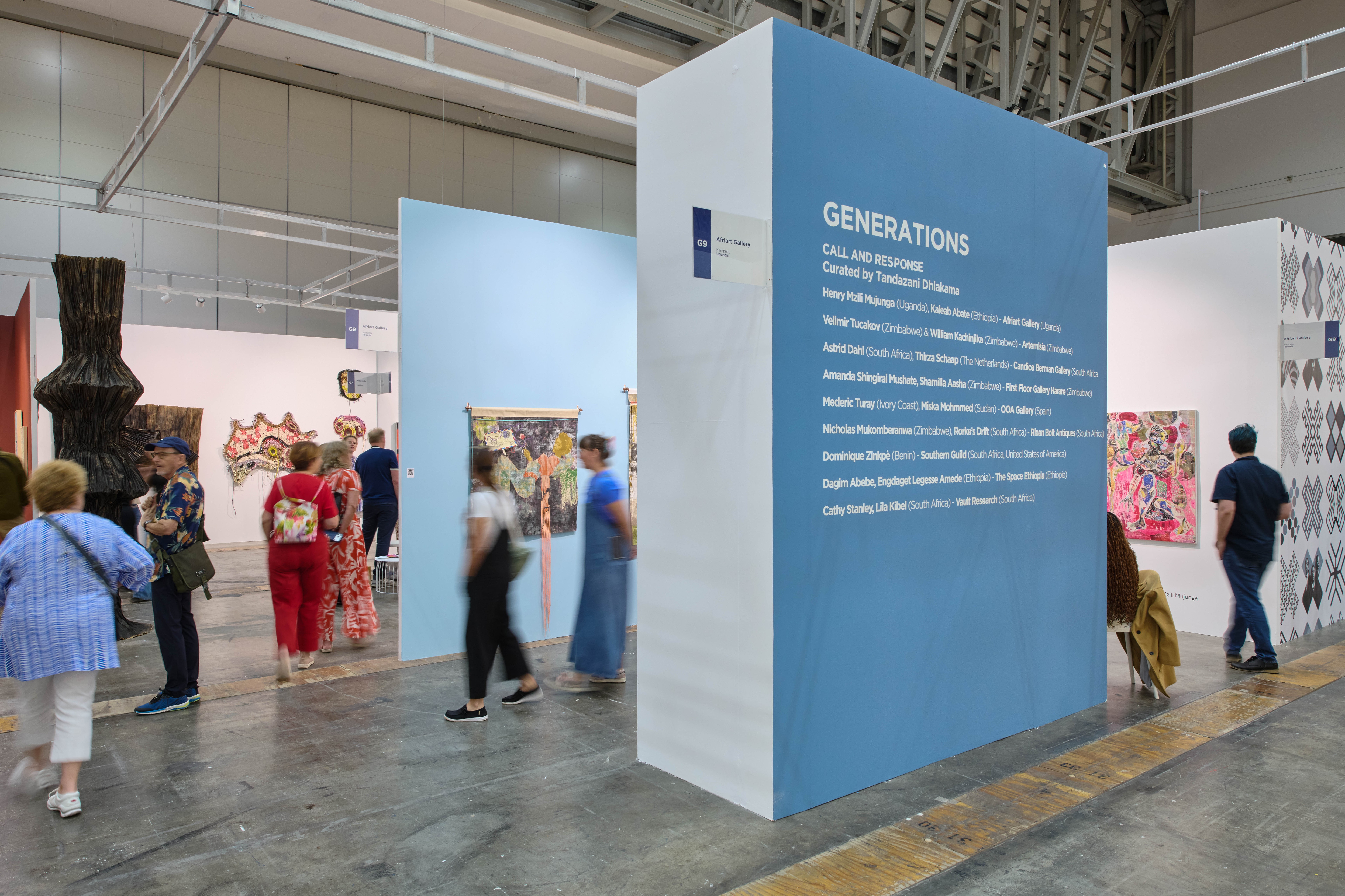 An art exhibition with visitors and a blue sign for the 'Generations' show.