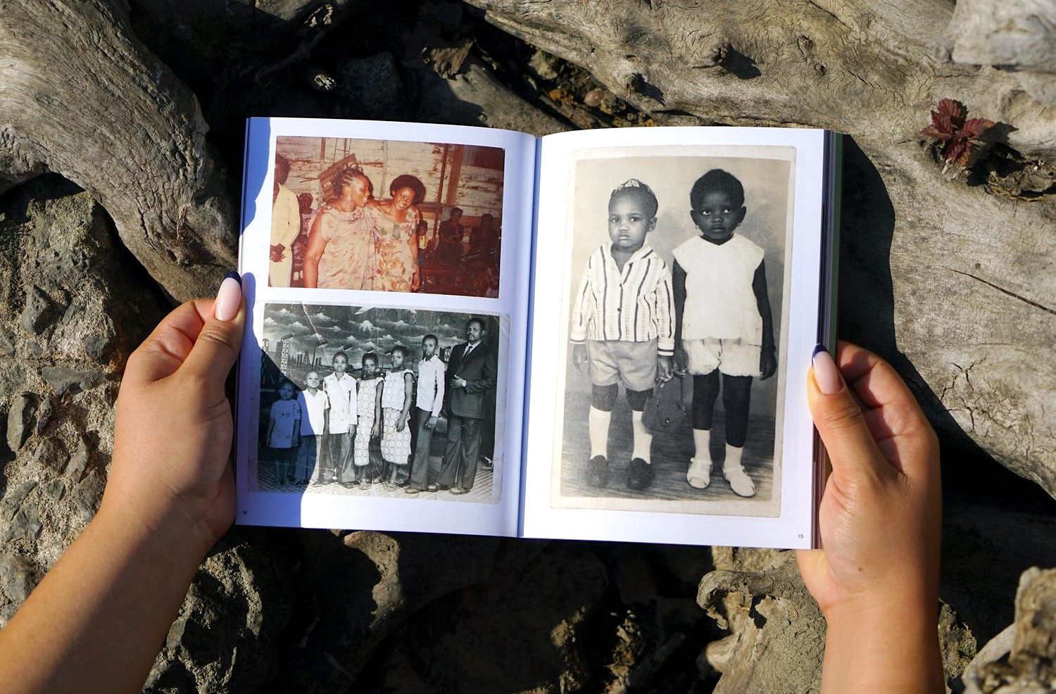 Hands hold an open book displaying old photographs, including a large black and white portrait of two children.
