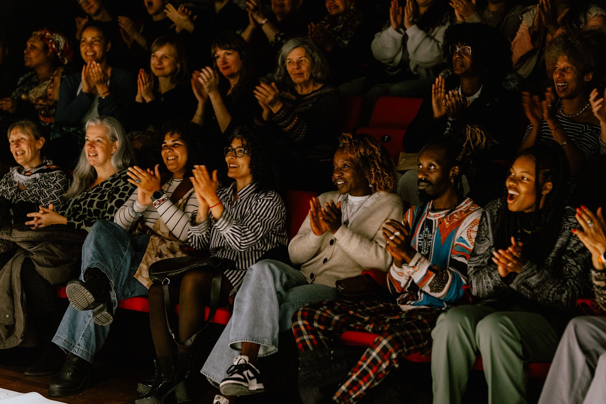 A diverse group of smiling people clapping in an audience.