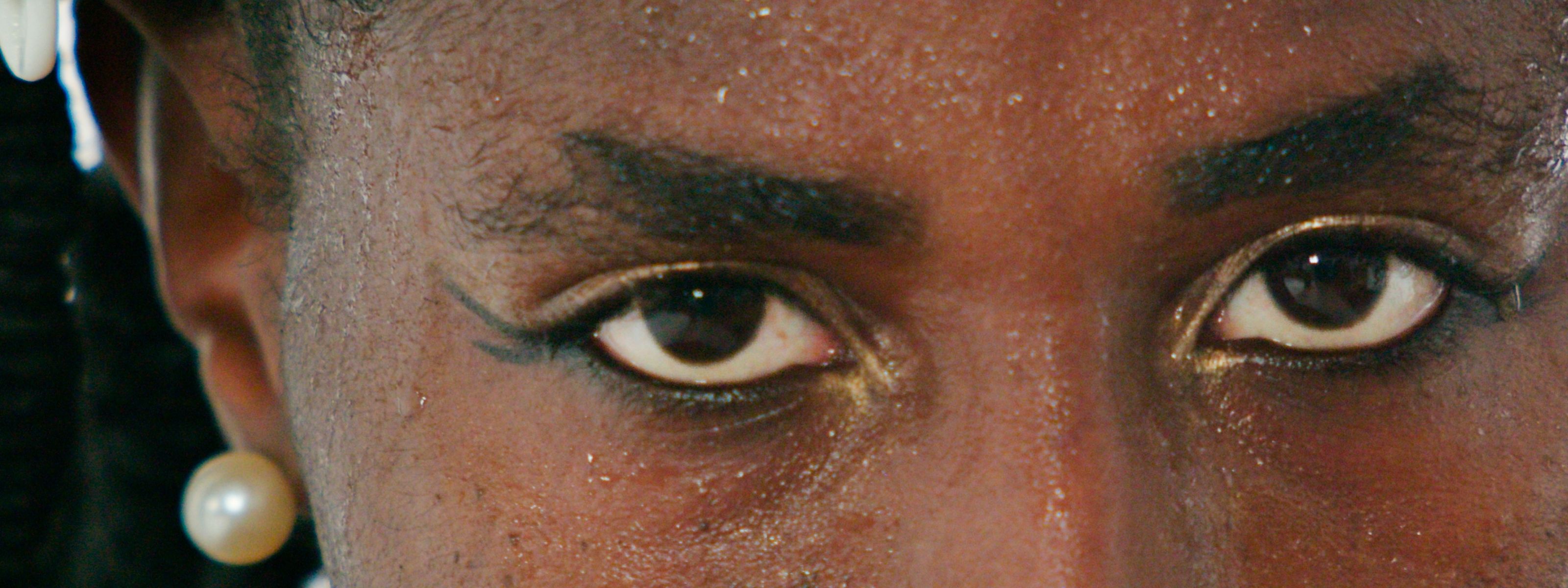 Close-up of eyes with winged eyeliner, gold glitter, and a pearl earring.