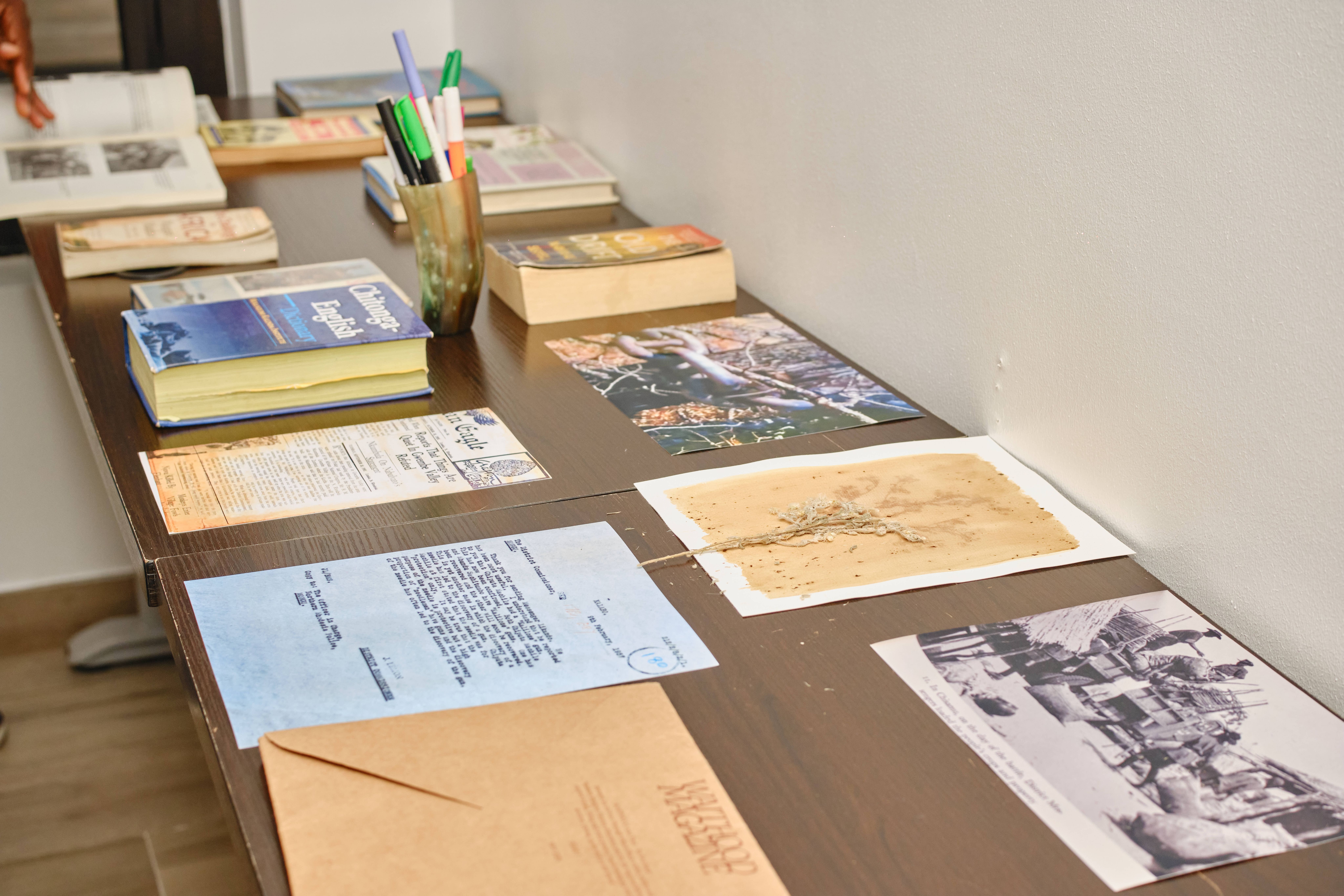 A table displaying books, historical documents, photographs, and a pressed plant specimen.
