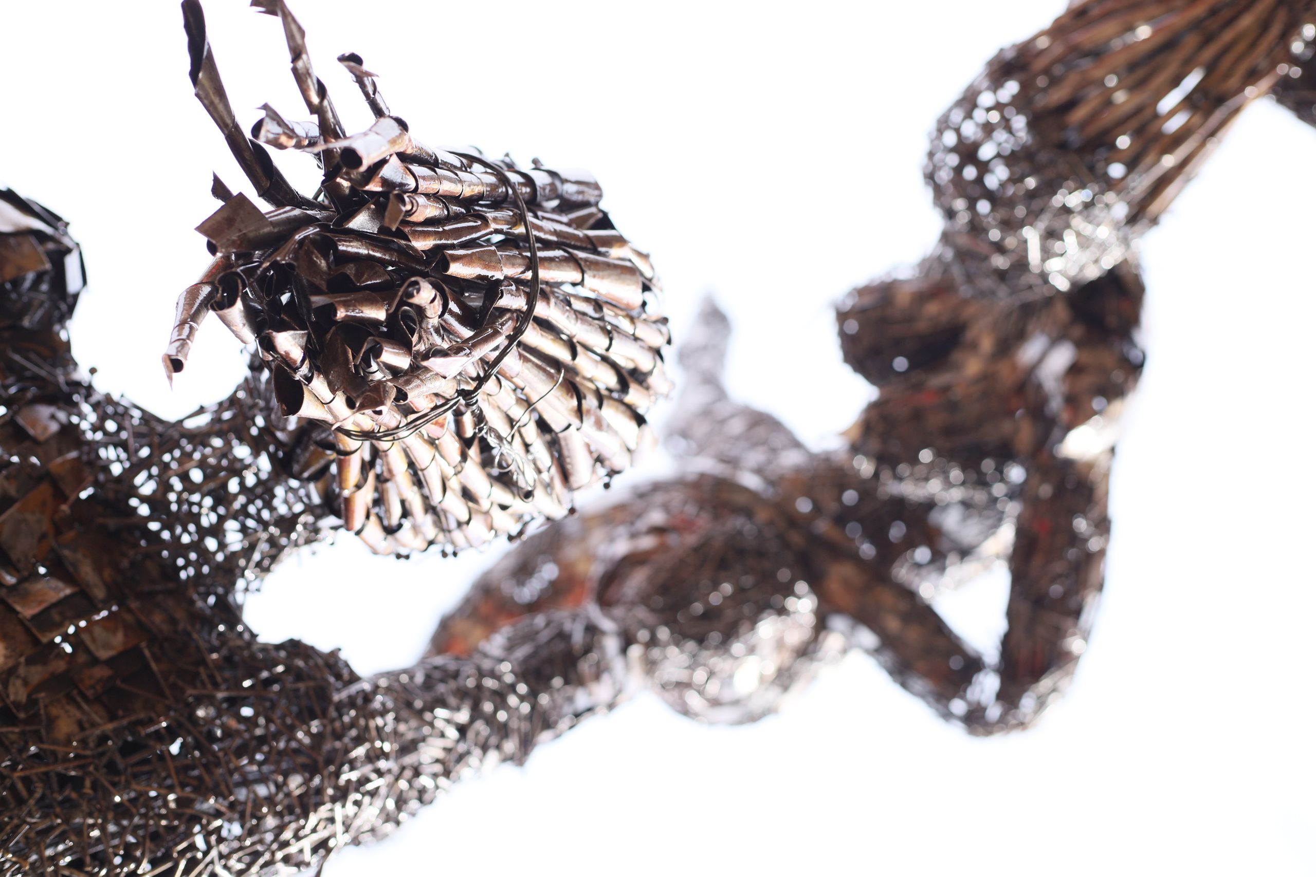 Abstract sculpture of intertwined forms made from dark, textured rolled metal pieces on a white background.