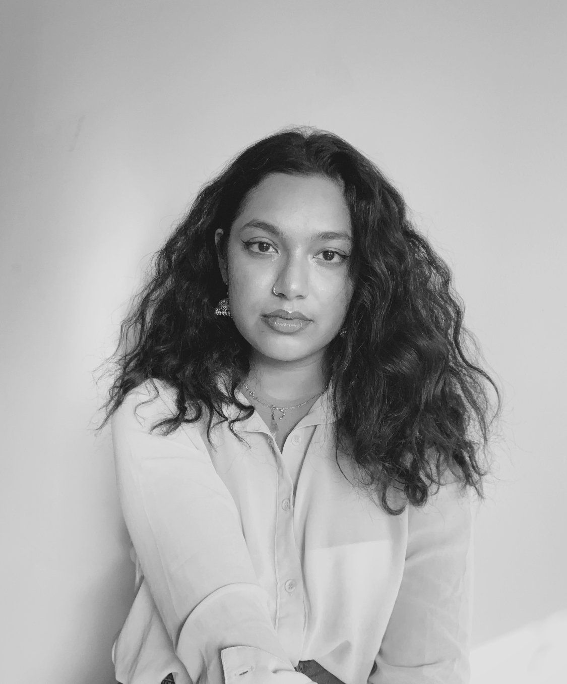 Black and white portrait of a woman with long curly hair, a nose ring, earrings, and a collared shirt.