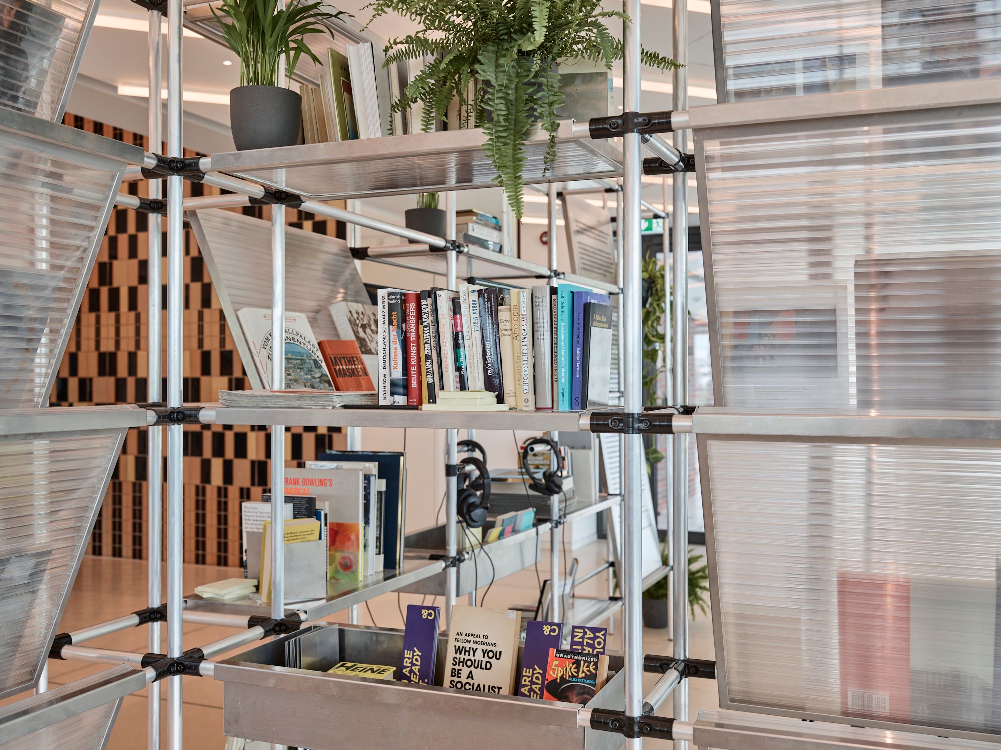A modern modular shelving unit with metal poles, translucent panels, books, and potted plants.