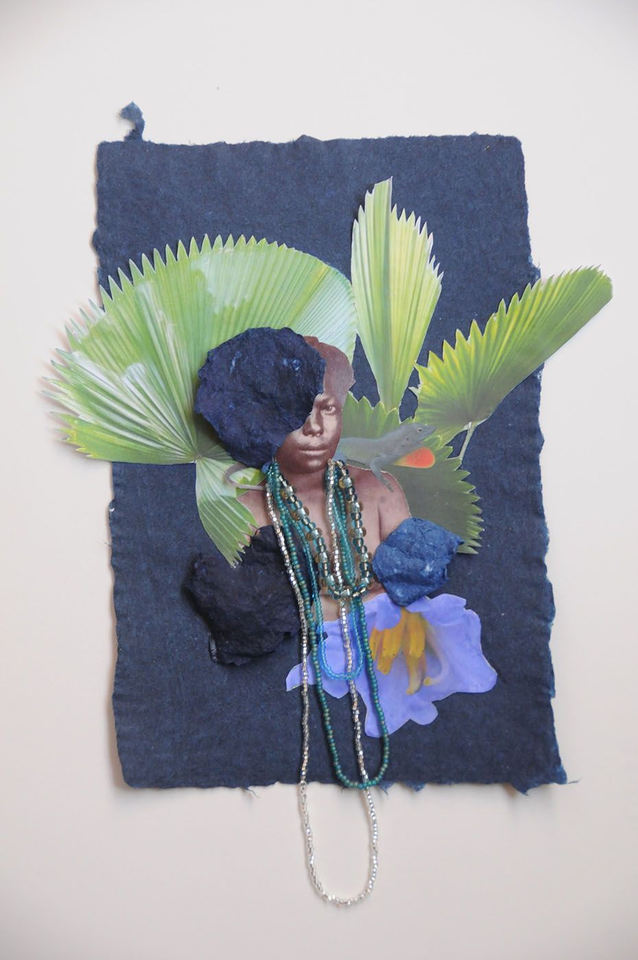 Collage of a person with beaded necklaces, green palm leaves, and textured blue elements on dark blue paper, with a purple flower.