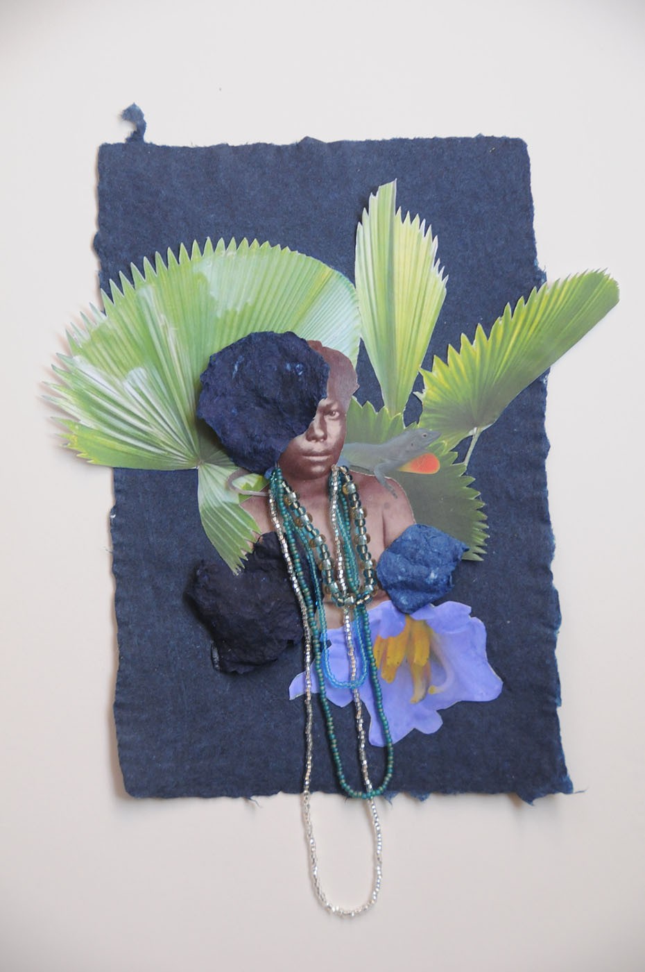 Collage of a person with beaded necklaces, green palm leaves, and textured blue elements on dark blue paper, with a purple flower.