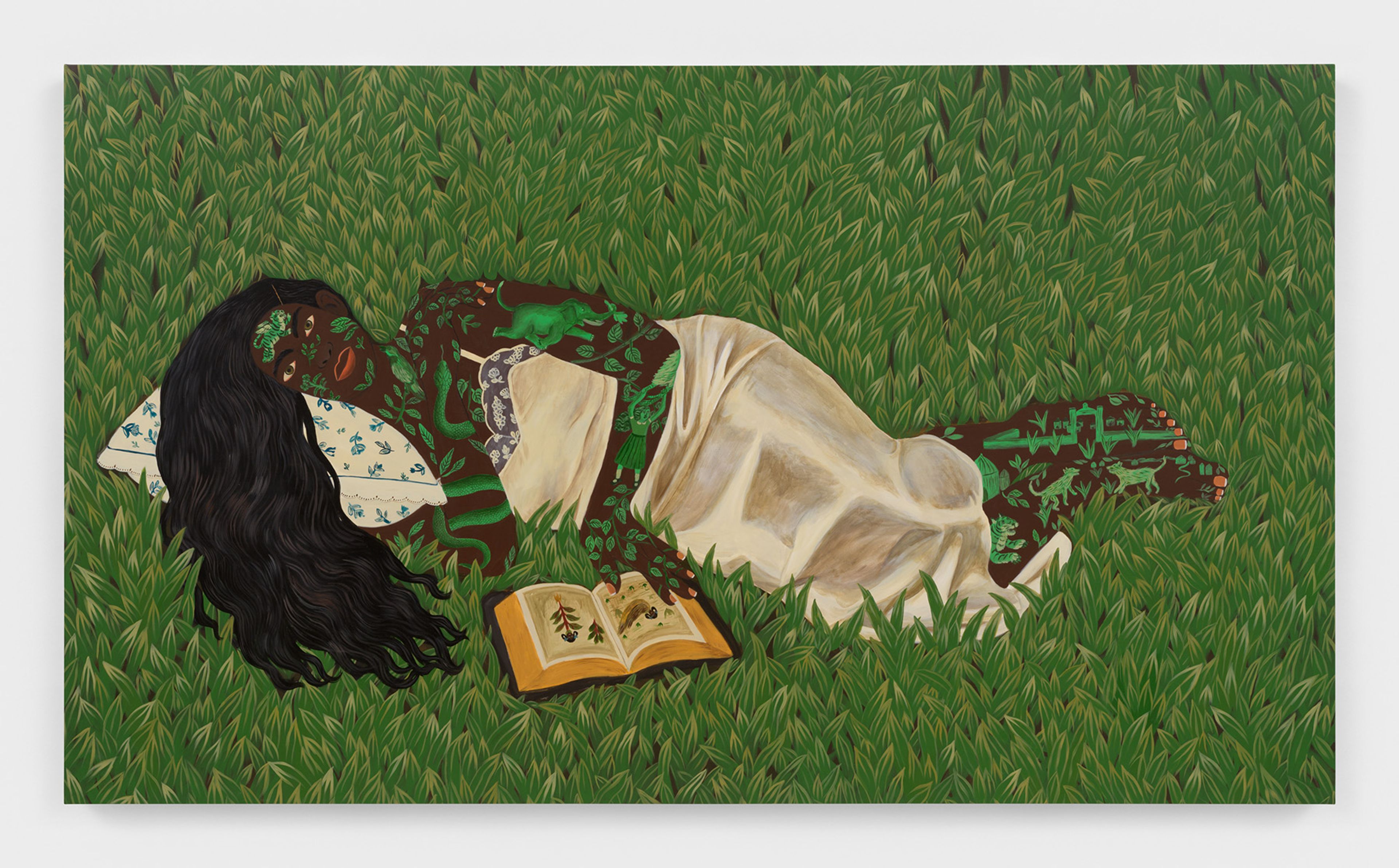 A painting of a person with long dark hair and dark skin patterned with green leaves and creatures, lying on a pillow in green grass with an open book.