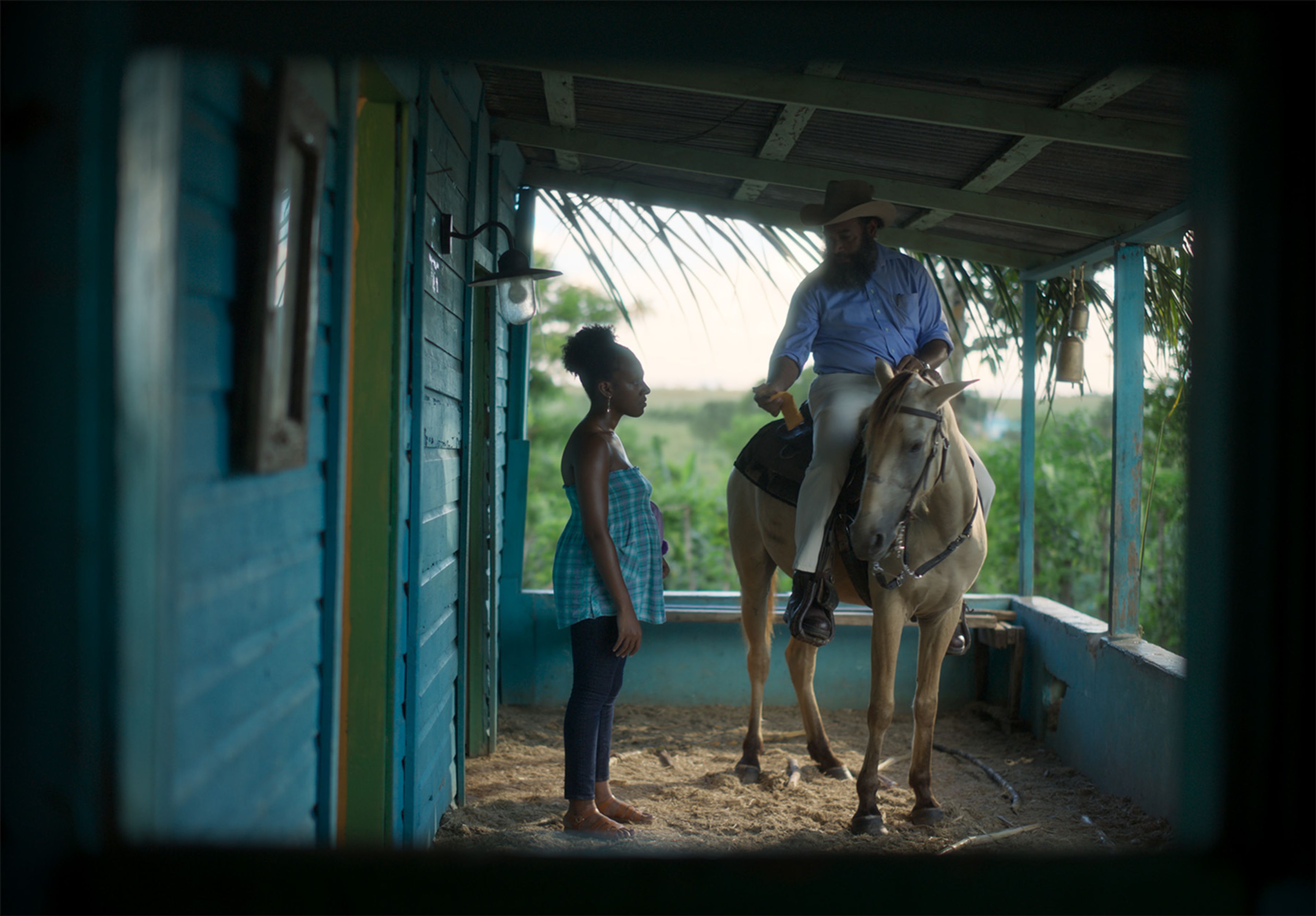 A man on a horse talks to a woman on a blue wooden porch.