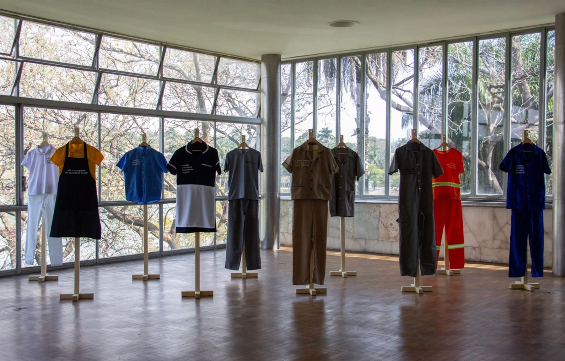 Diverse work uniforms displayed on stands in a bright room with large windows.