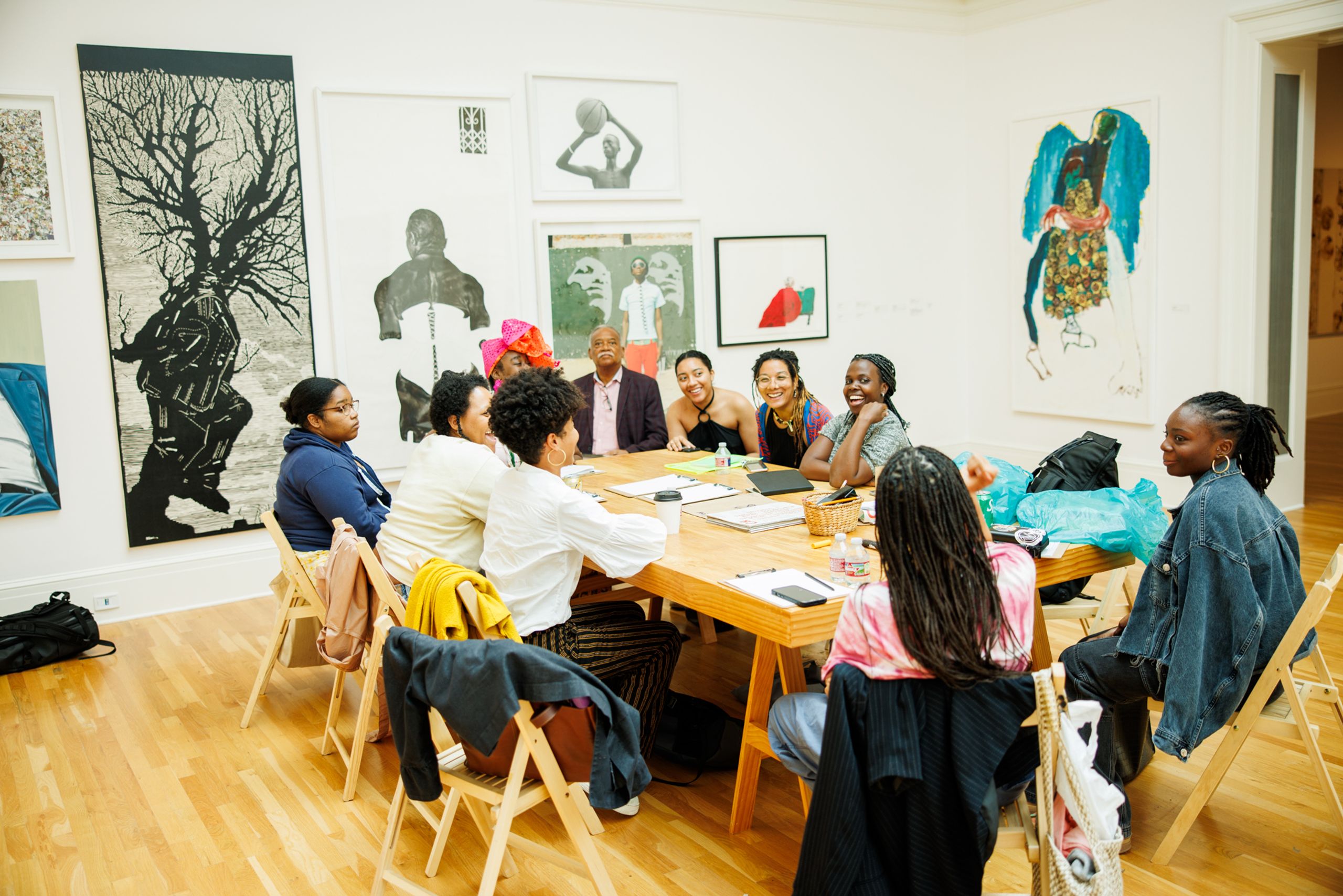 A diverse group of people, mostly women, discuss around a table in an art gallery.