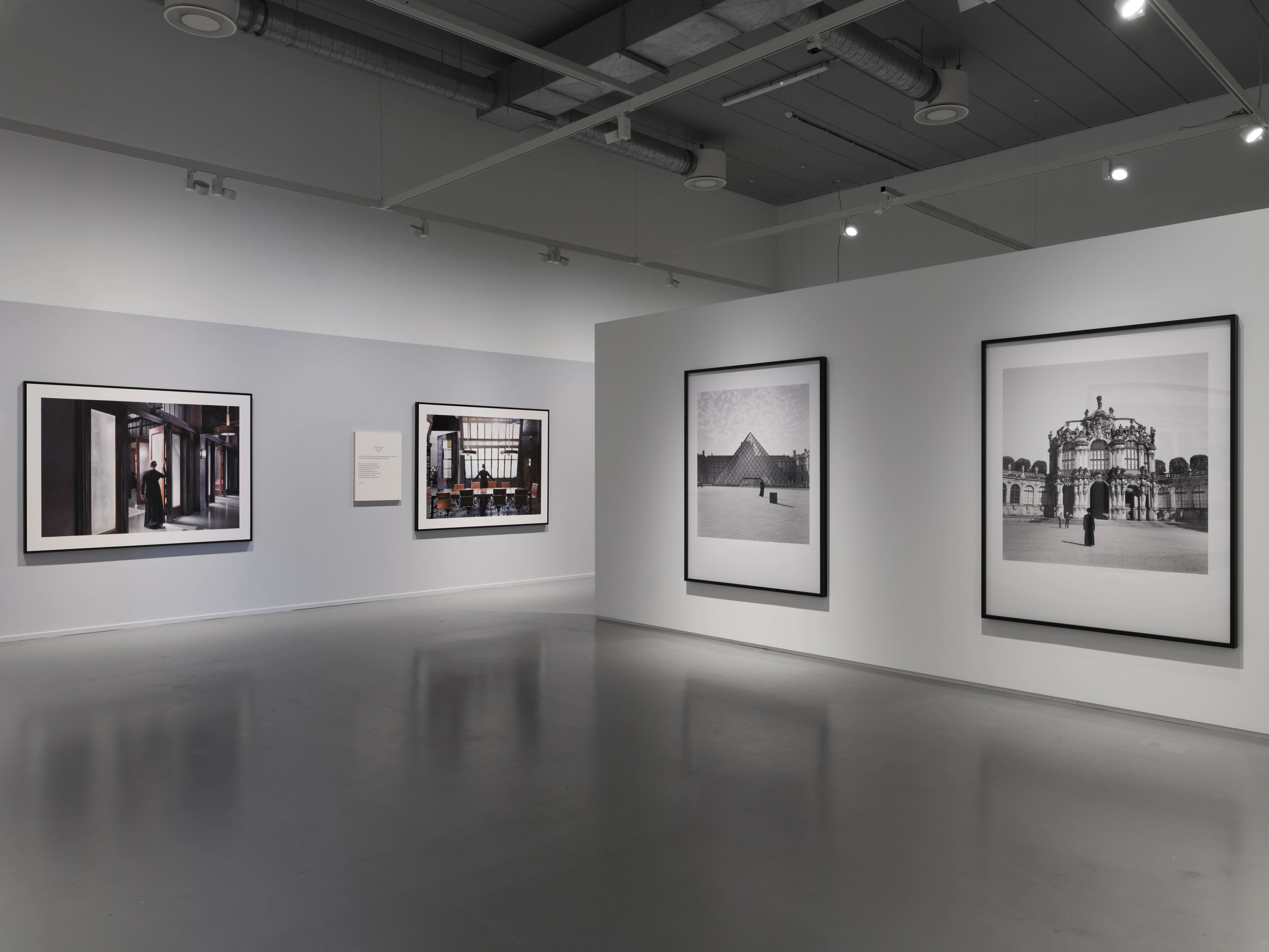 A modern art gallery features four framed photographs on white and light gray walls, two in color and two in black and white.