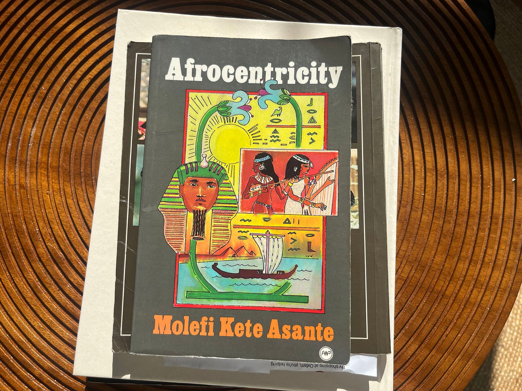 A book titled Afrocentricity by Molefi Kete Asante, featuring an Egyptian-themed cover illustration, lies on a wooden table.