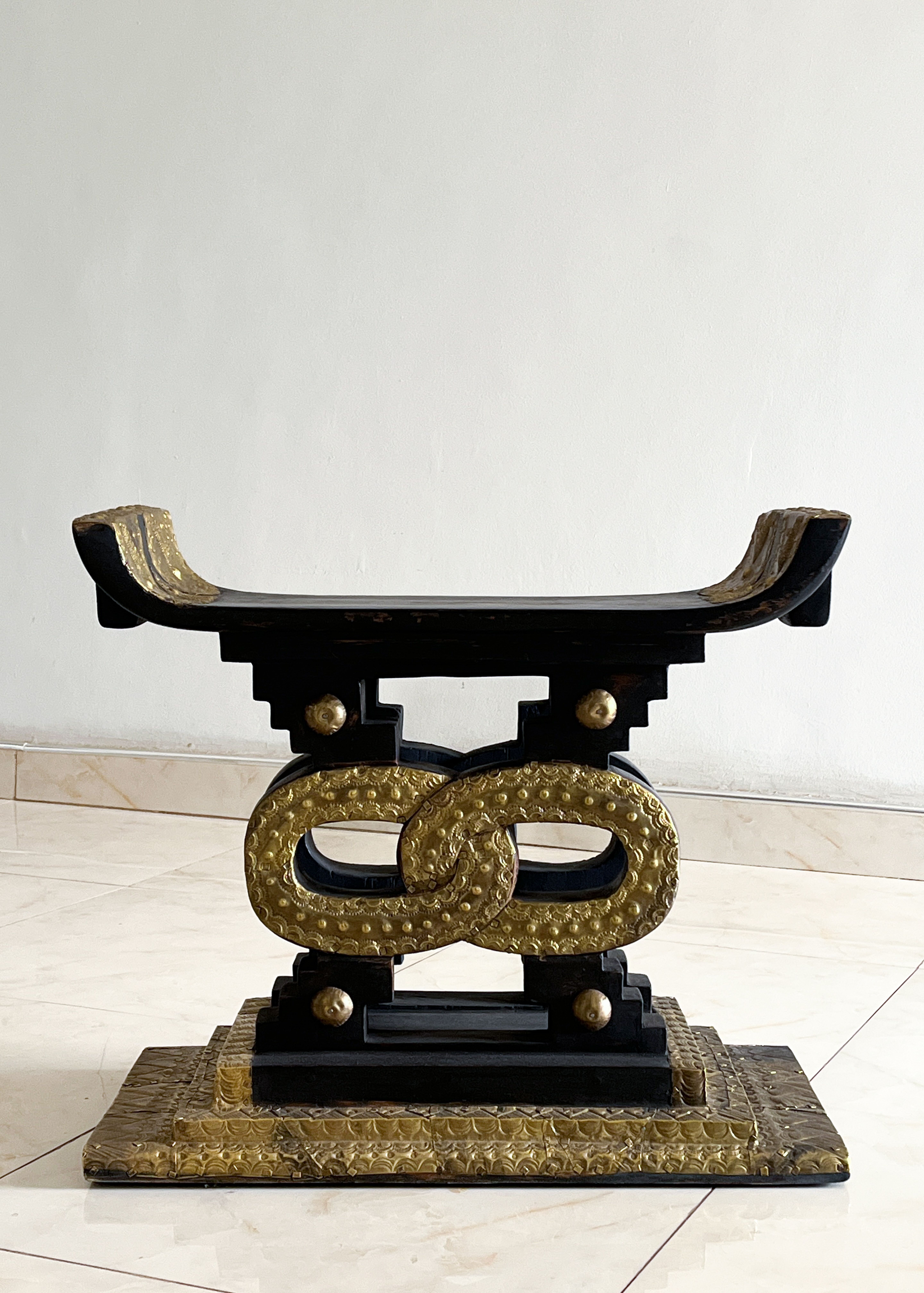 Black and gold Ashanti stool with a curved seat and textured, intertwining gold oval supports.