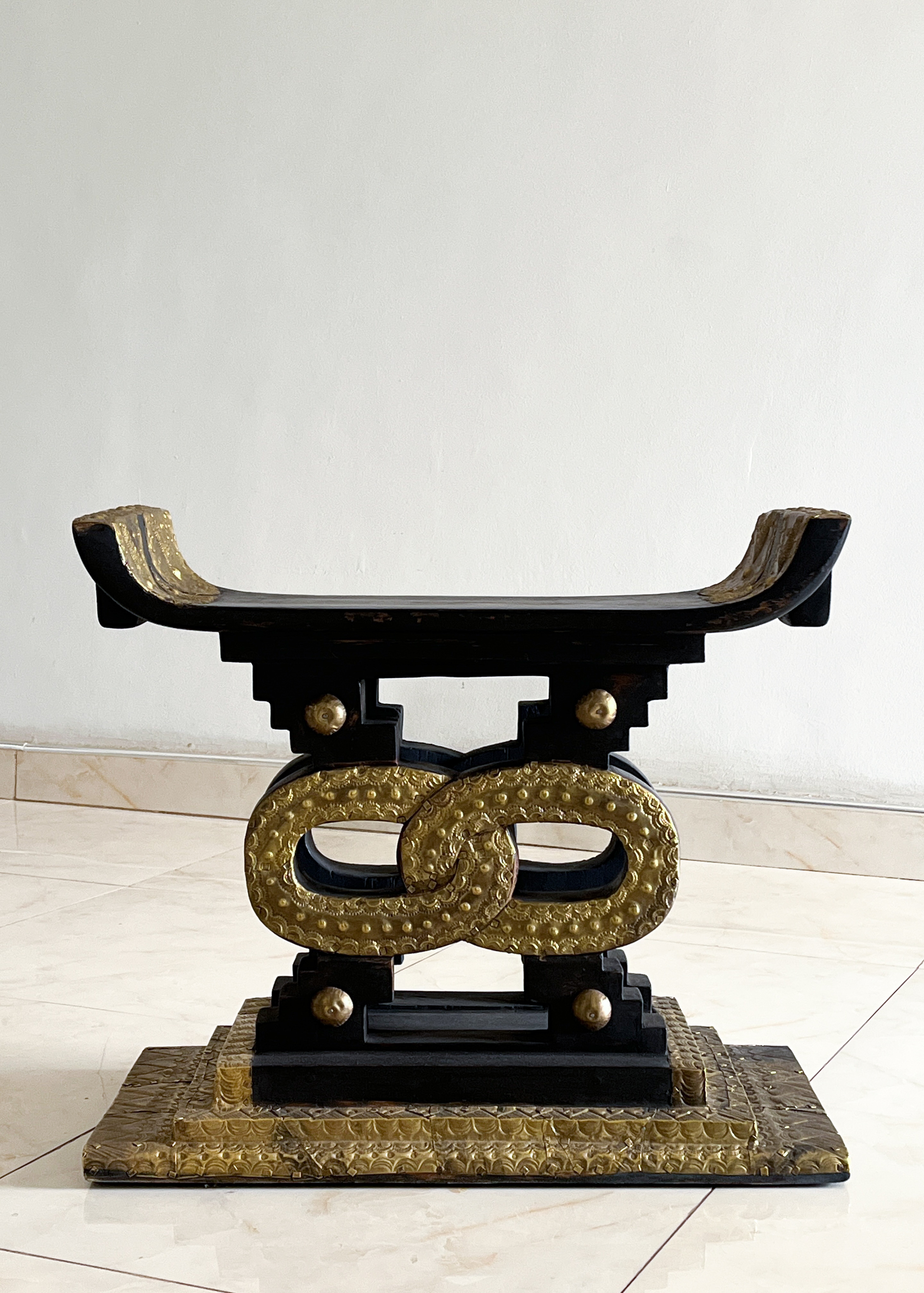 Black and gold Ashanti stool with a curved seat and textured, intertwining gold oval supports.