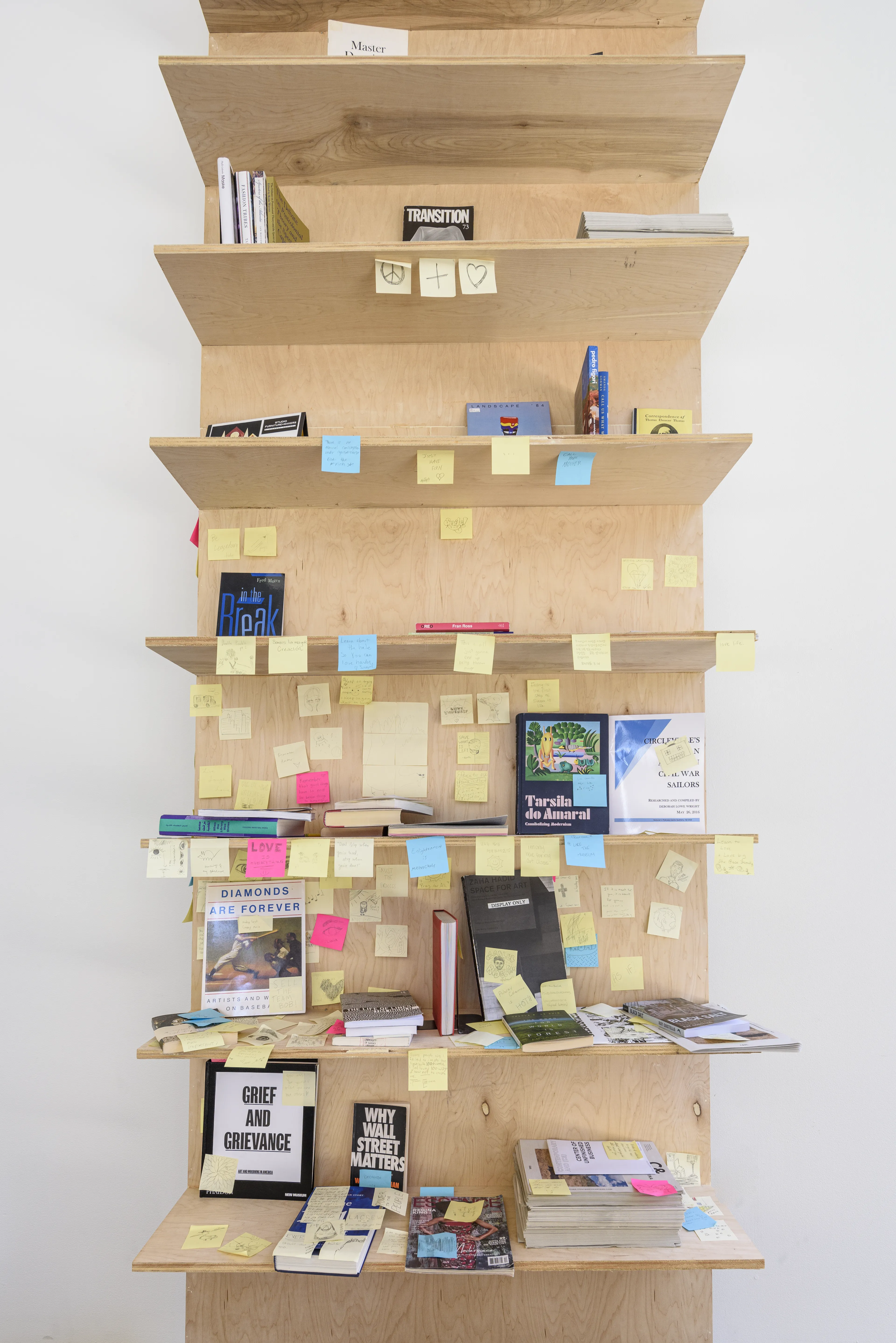 A tall plywood shelving unit filled with books and magazines, heavily covered in colorful sticky notes.
