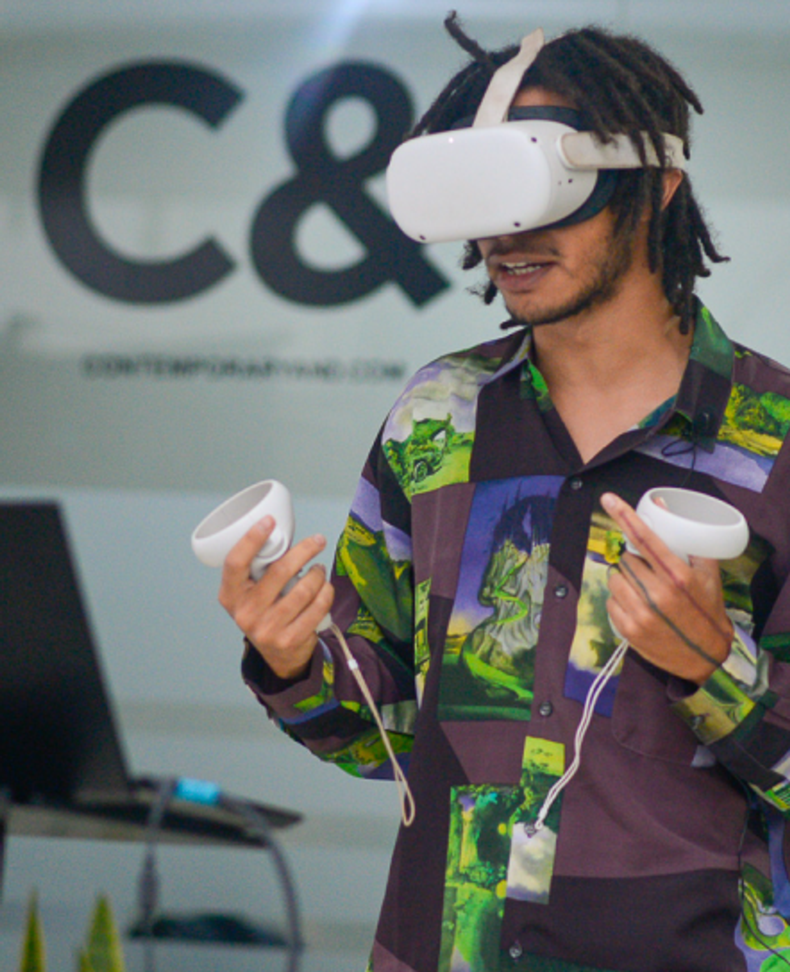 A person with dreadlocks wearing a white VR headset and holding two white controllers.