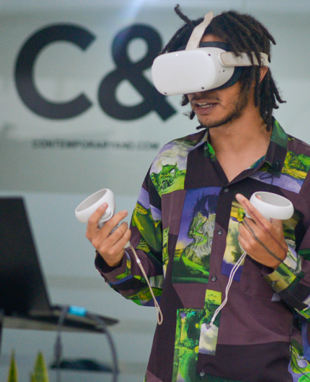A person with dreadlocks wearing a white VR headset and holding two white controllers.