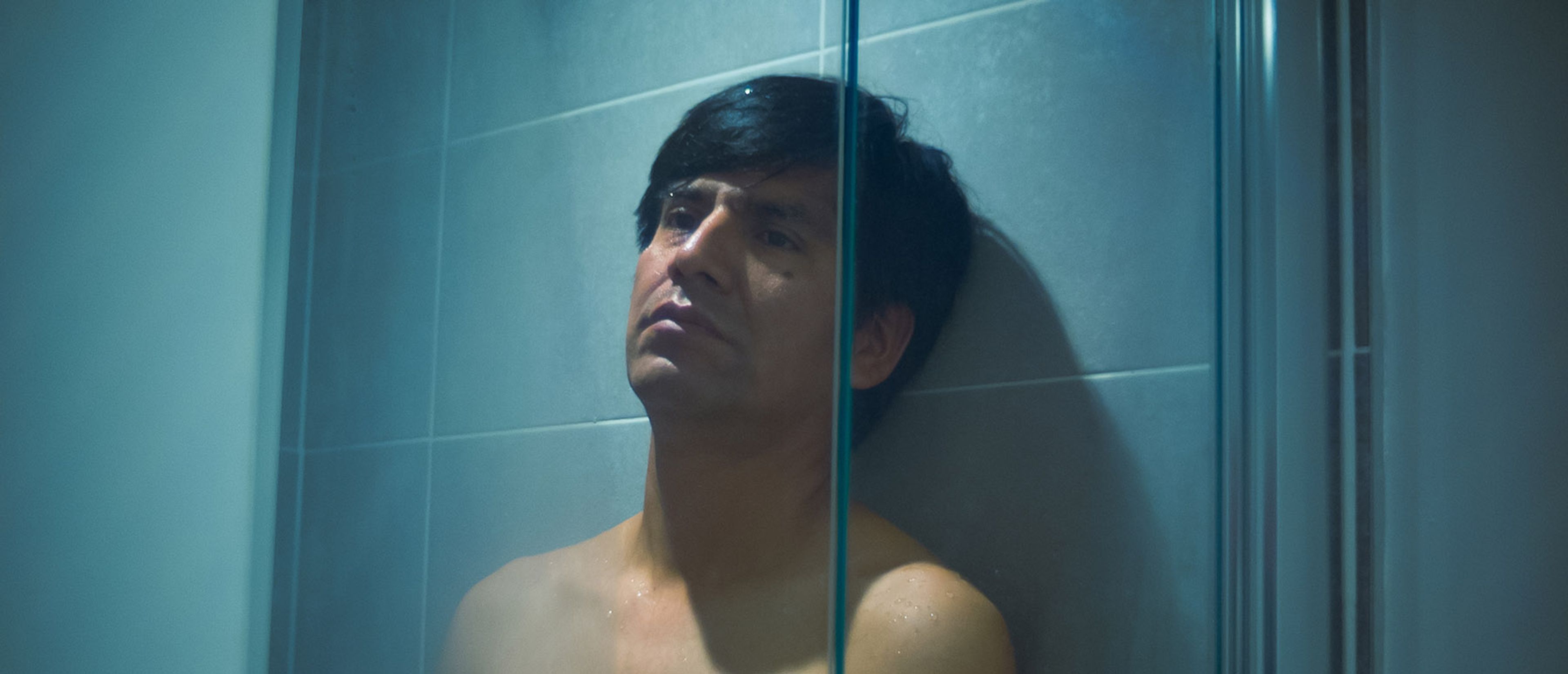 A wet, bare-chested man looking pensive in a shower.