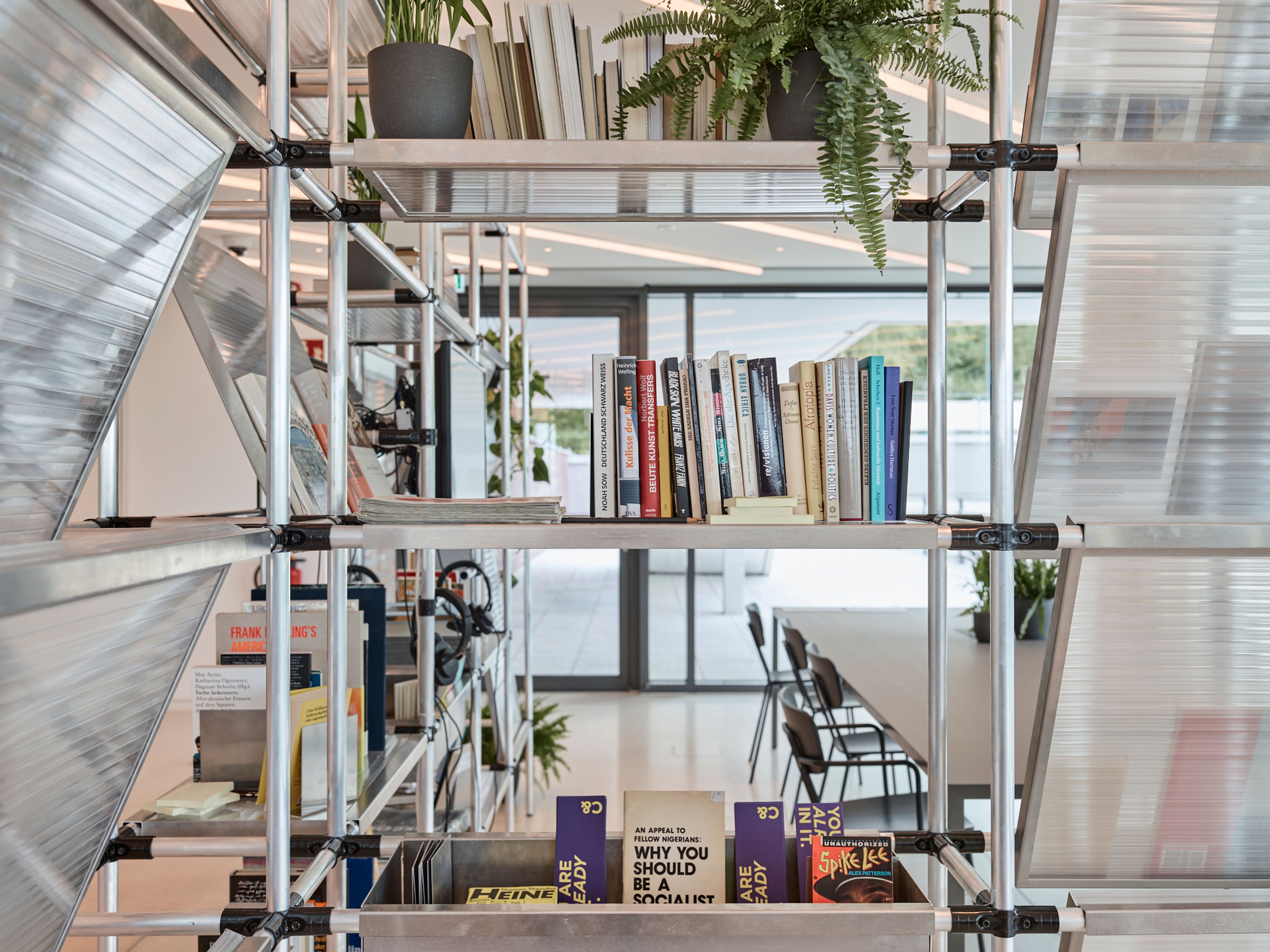 A modern industrial-style metal shelving unit with books and plants, serving as a room divider in a bright office.