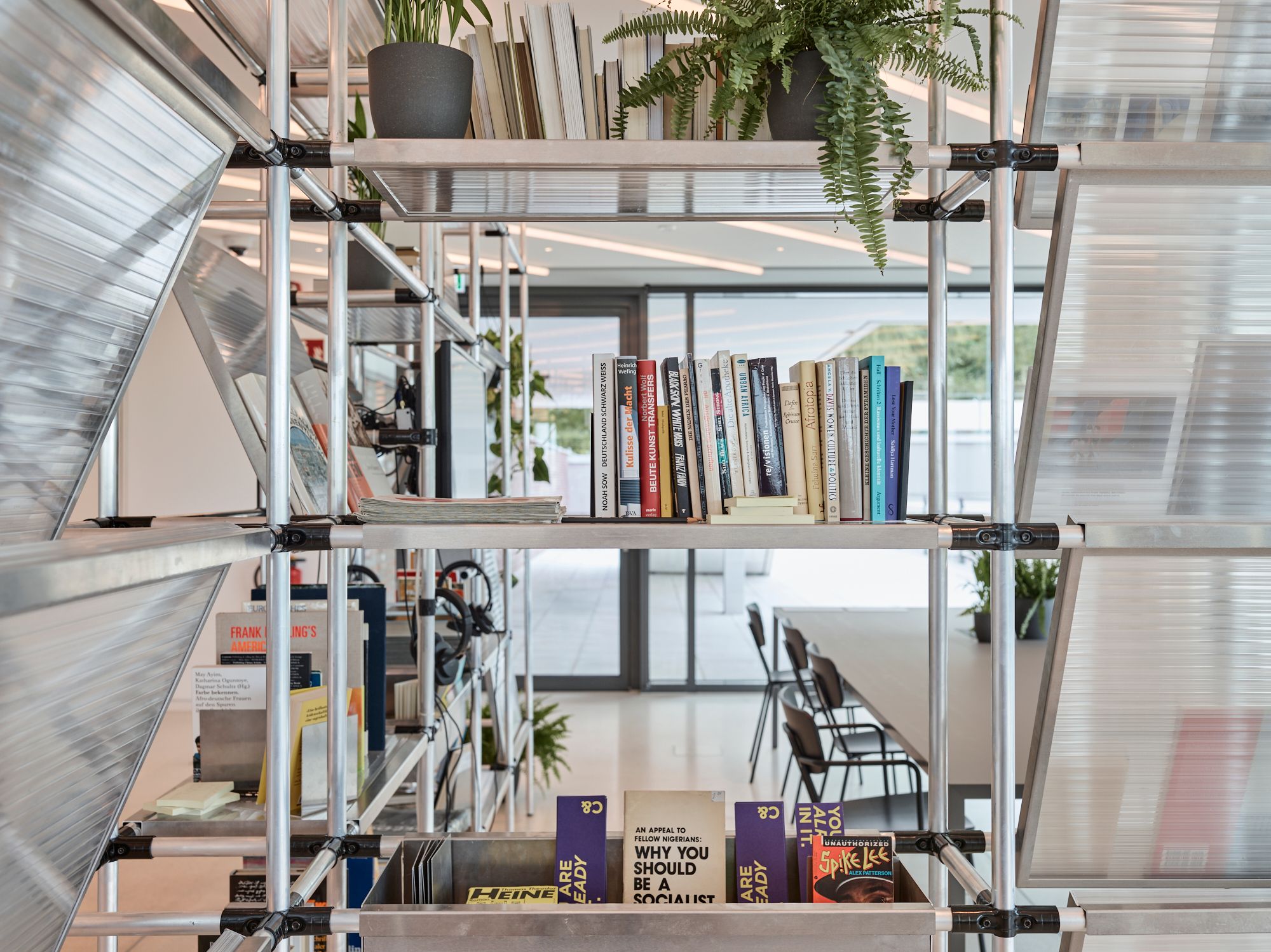 A modern industrial-style metal shelving unit with books and plants, serving as a room divider in a bright office.
