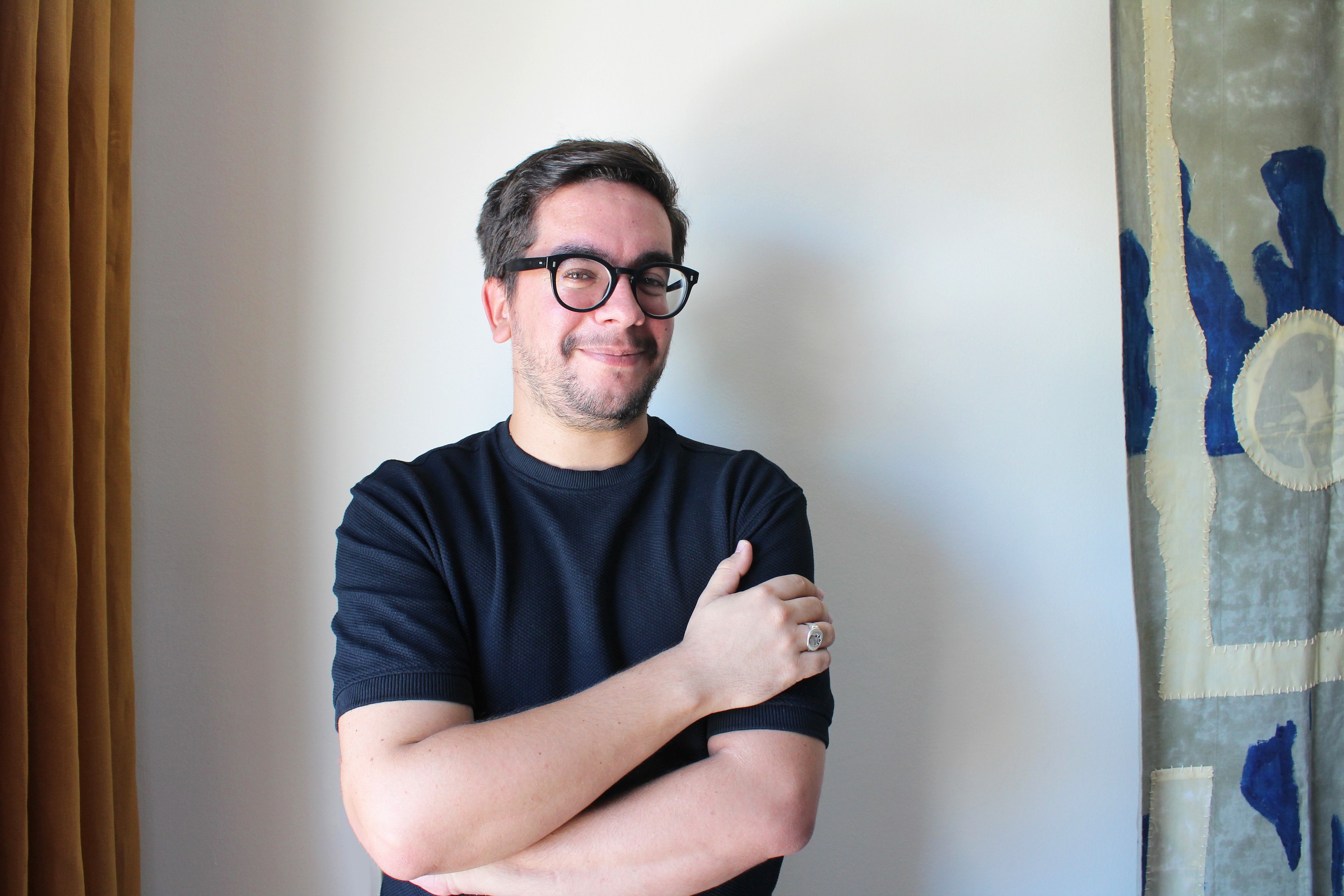 Smiling man with dark hair, glasses, and a beard, wearing a black shirt and crossing his arms.
