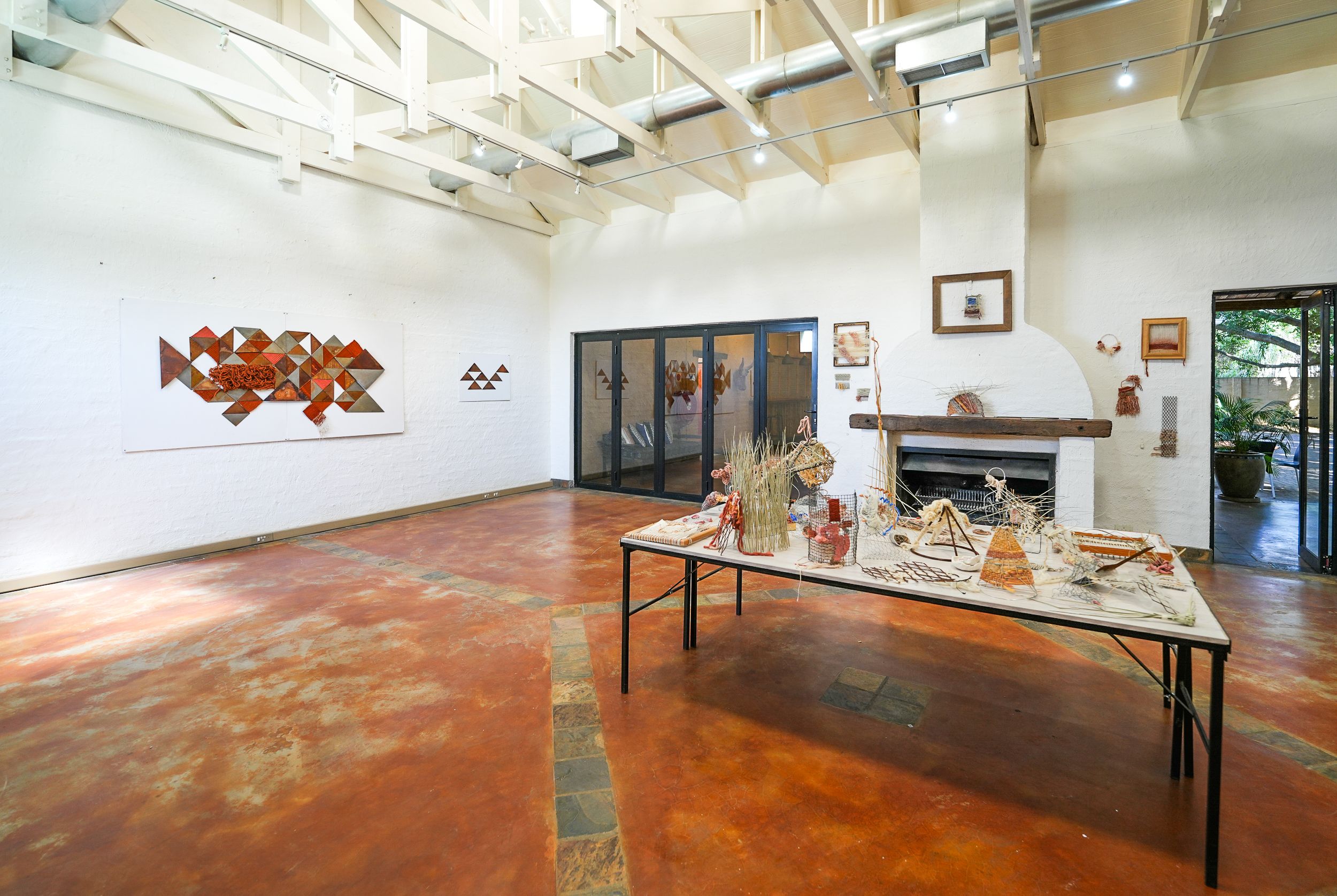 An art gallery space featuring a long table of various crafts, abstract geometric wall art, and a large fireplace.