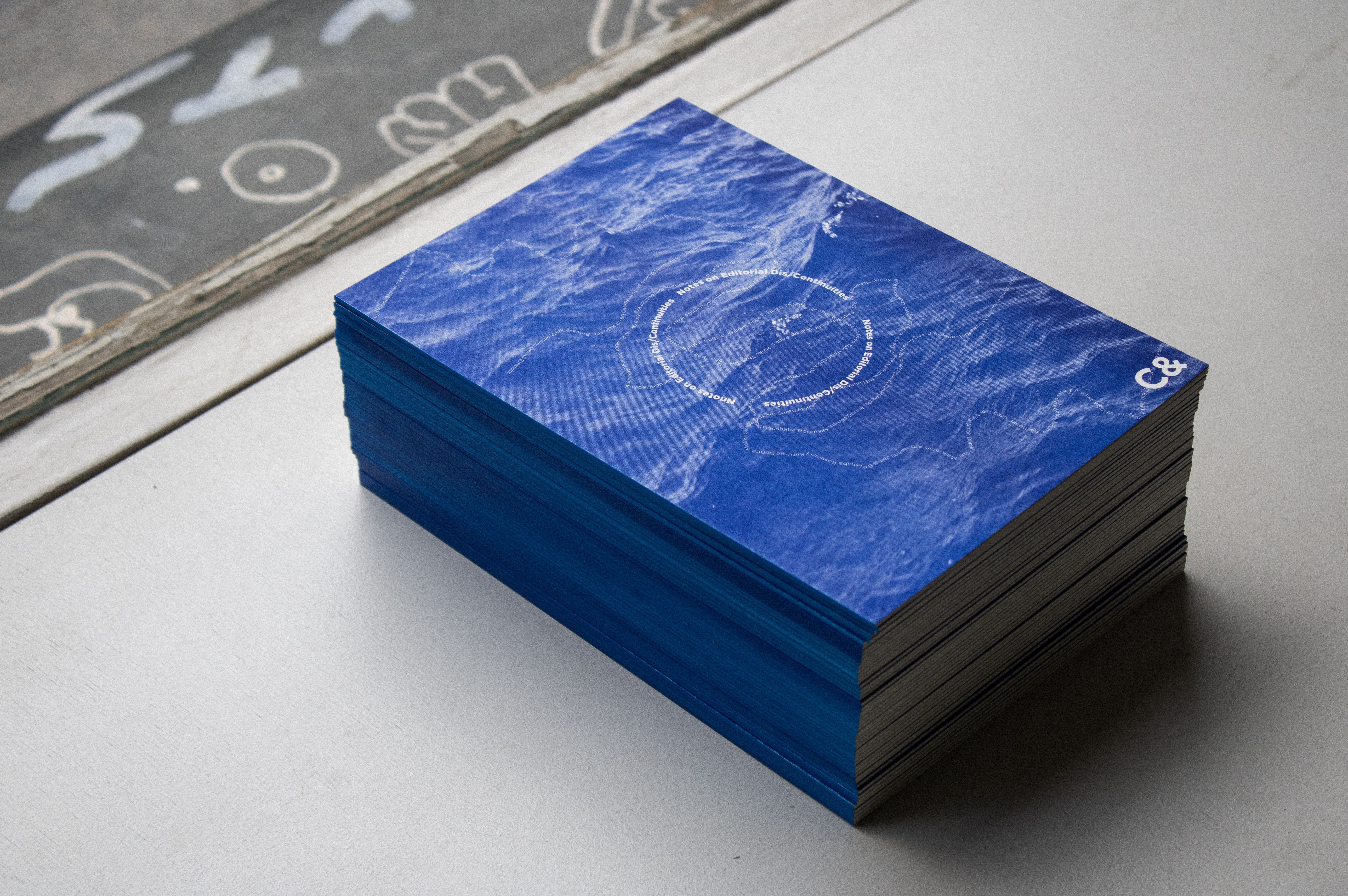 Stack of publications with a water ripple design and 'C&' logo, featuring blue colored edges.