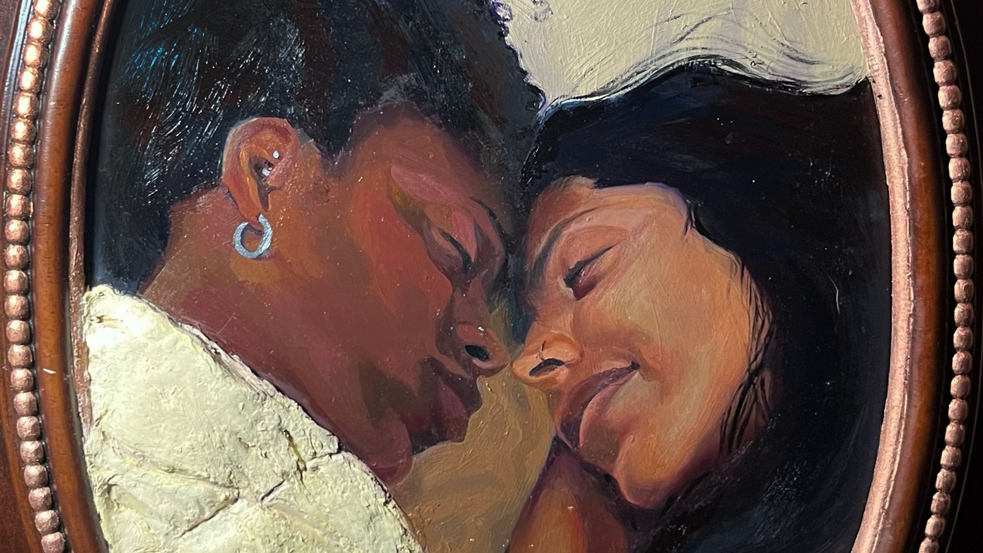 Painting in an oval frame showing two people with closed eyes, their faces close together in a tender moment.
