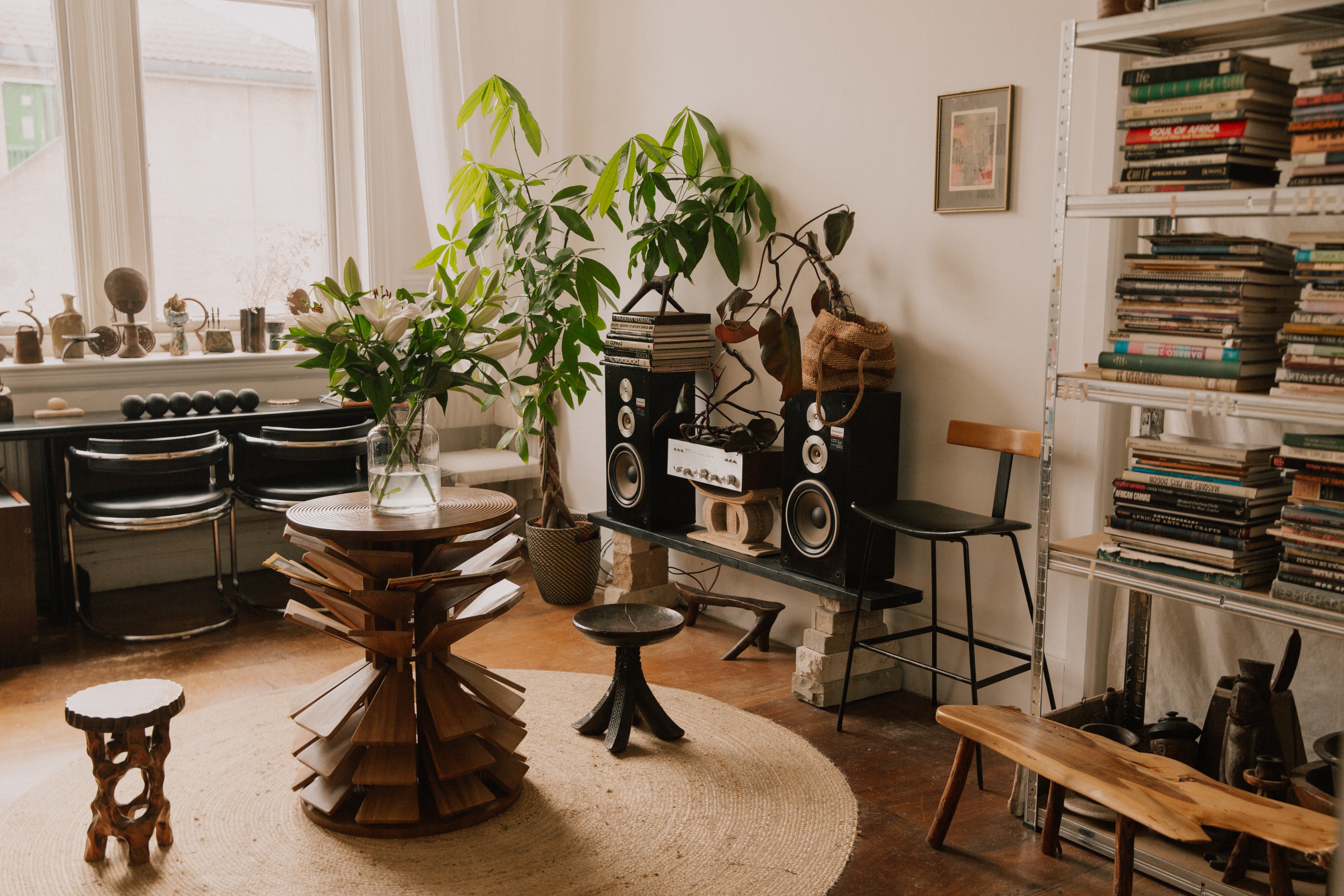 Eclectic living room with a large plant, full bookshelves, a stereo system, and unique wooden furniture on a round jute rug.