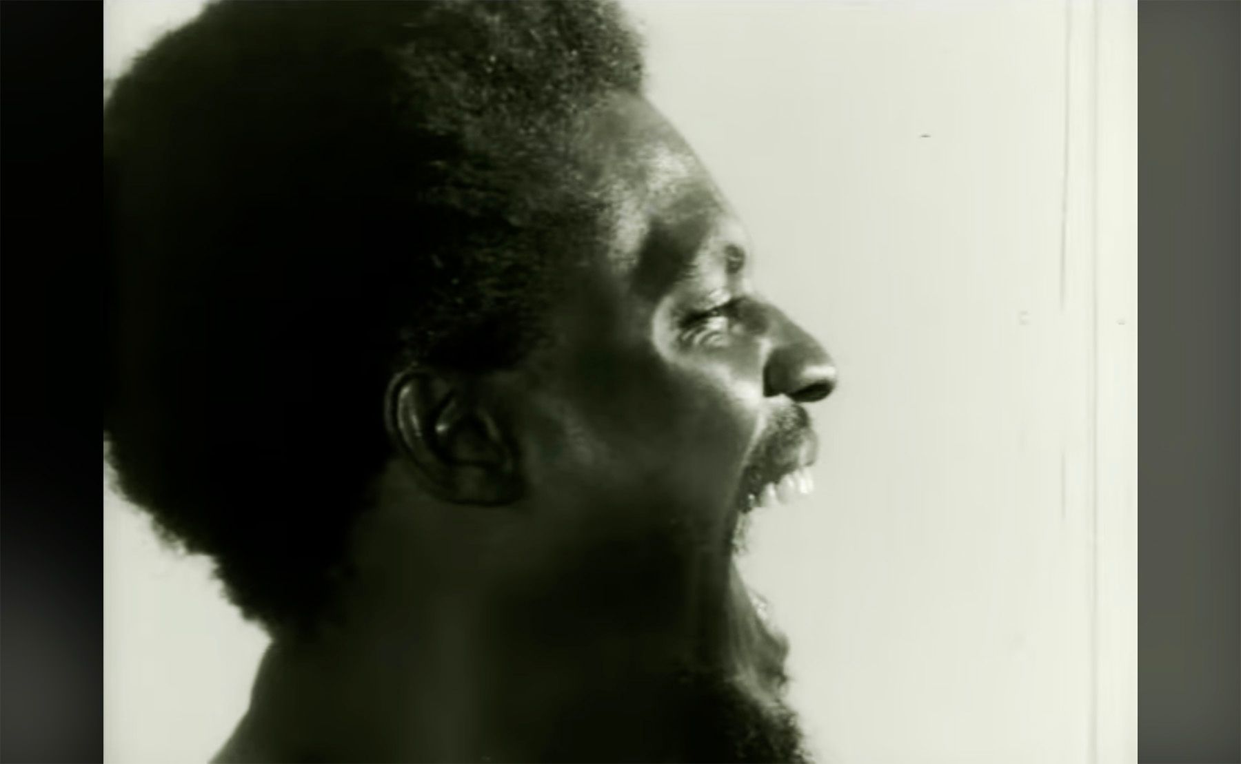 Monochrome profile of a screaming man with textured hair and a beard.