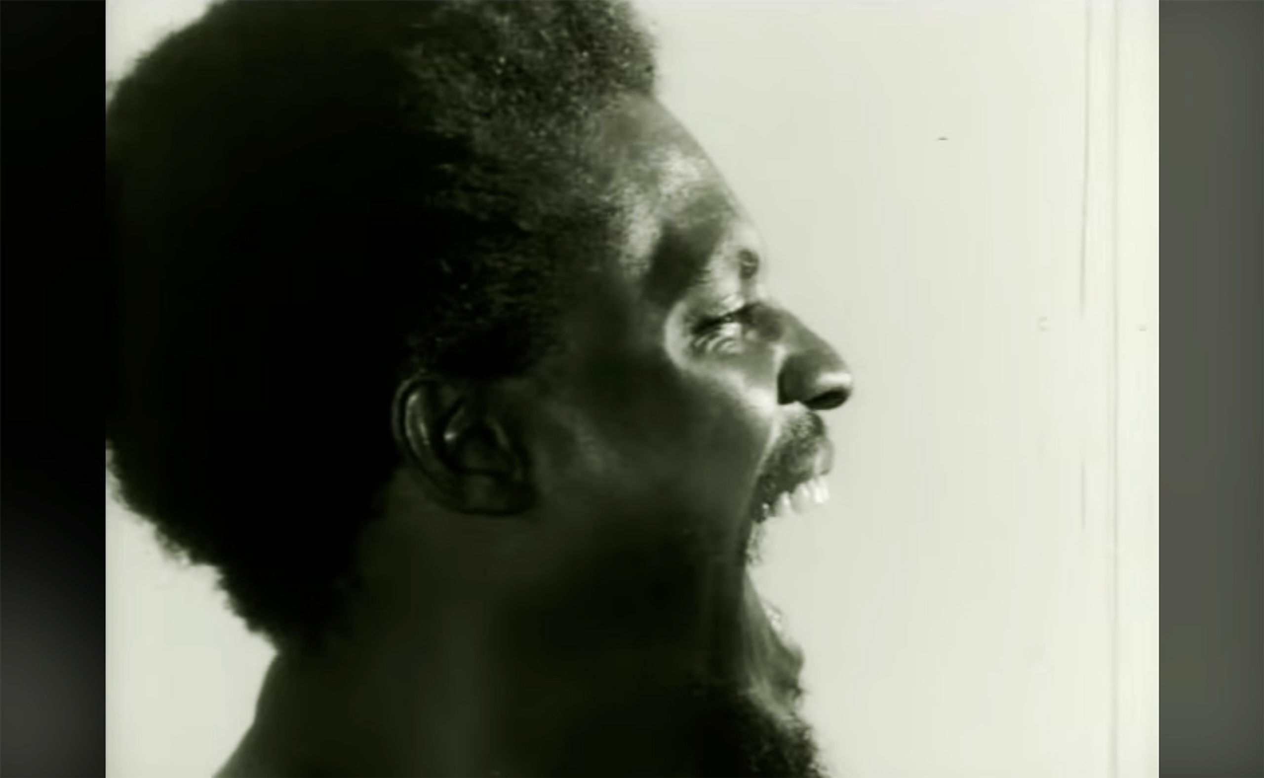 Monochrome profile of a screaming man with textured hair and a beard.