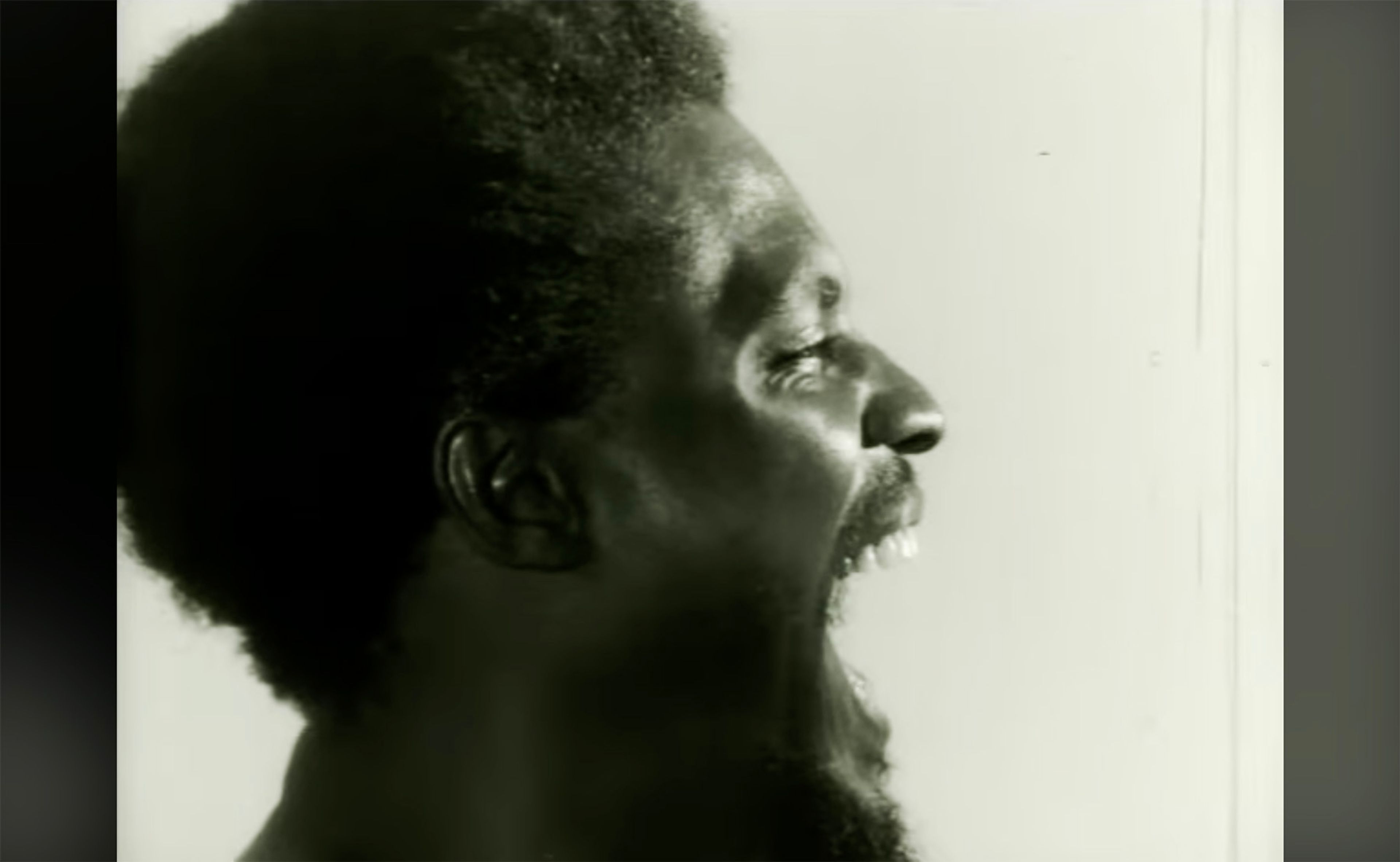 Monochrome profile of a screaming man with textured hair and a beard.