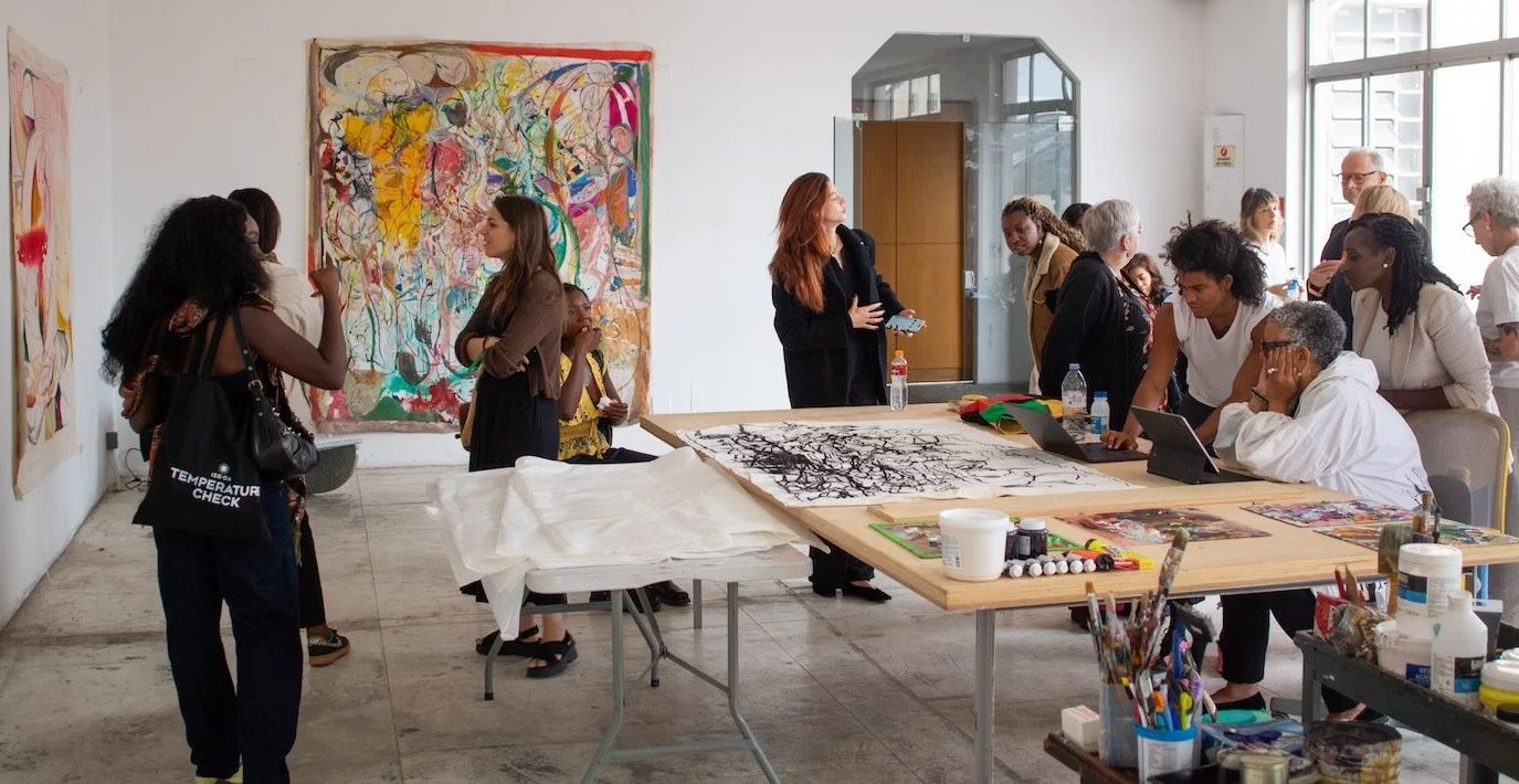 A lively art studio with diverse people, large abstract paintings on walls, and art projects on tables.