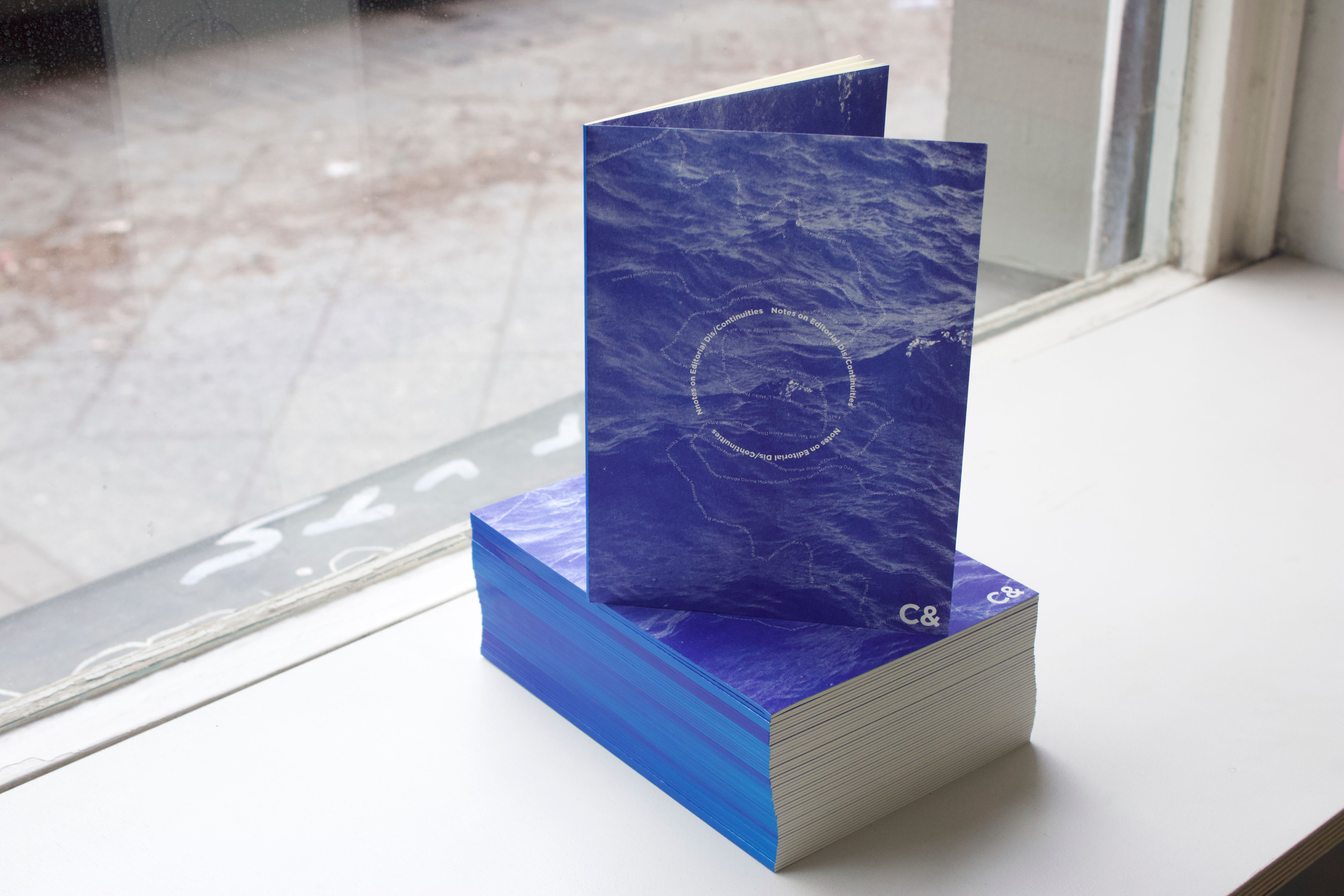 A stack of blue publications with a wavy pattern, one standing upright, on a white windowsill.