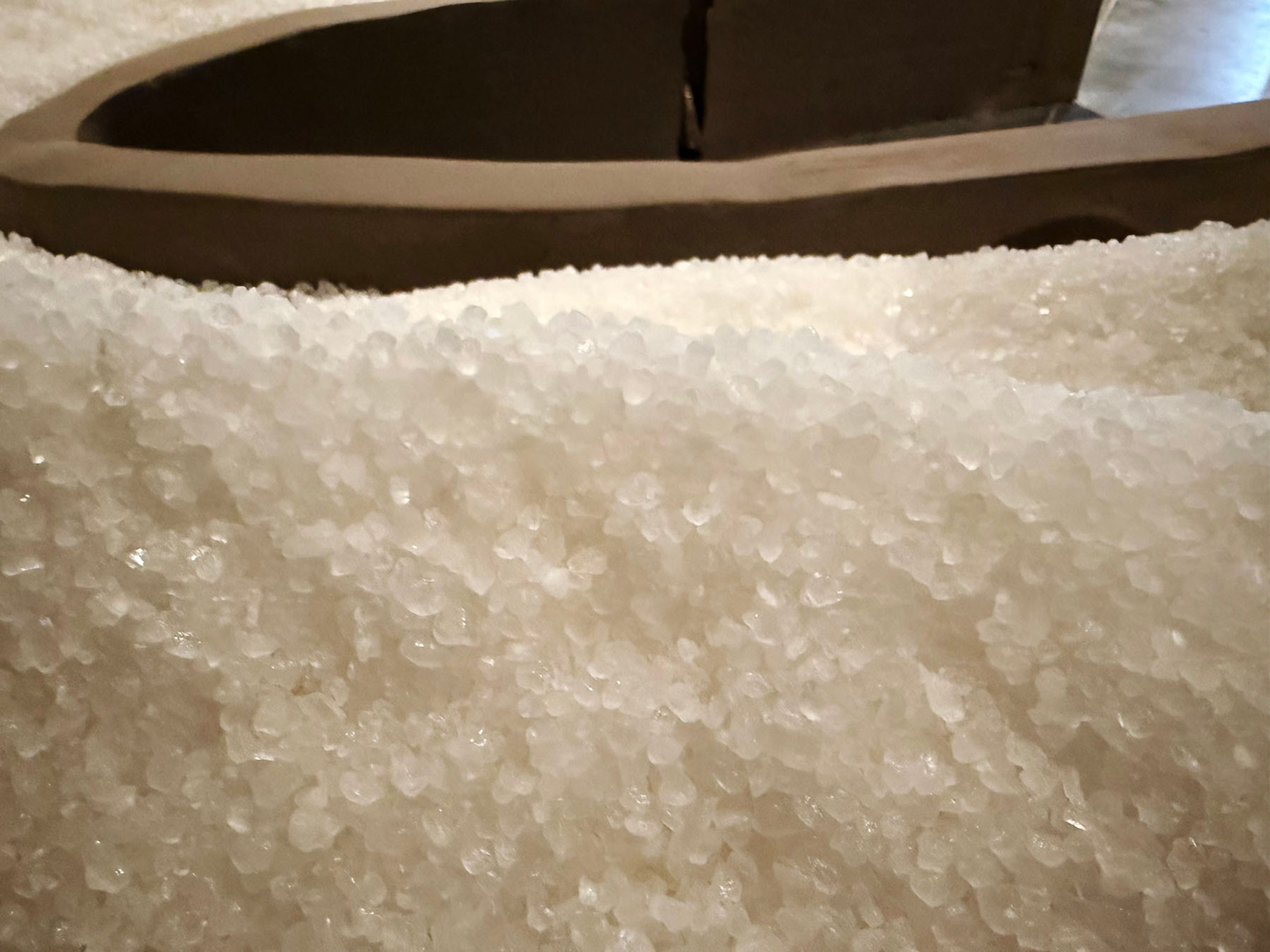 Mound of translucent white crystals with a dark, curved object behind.