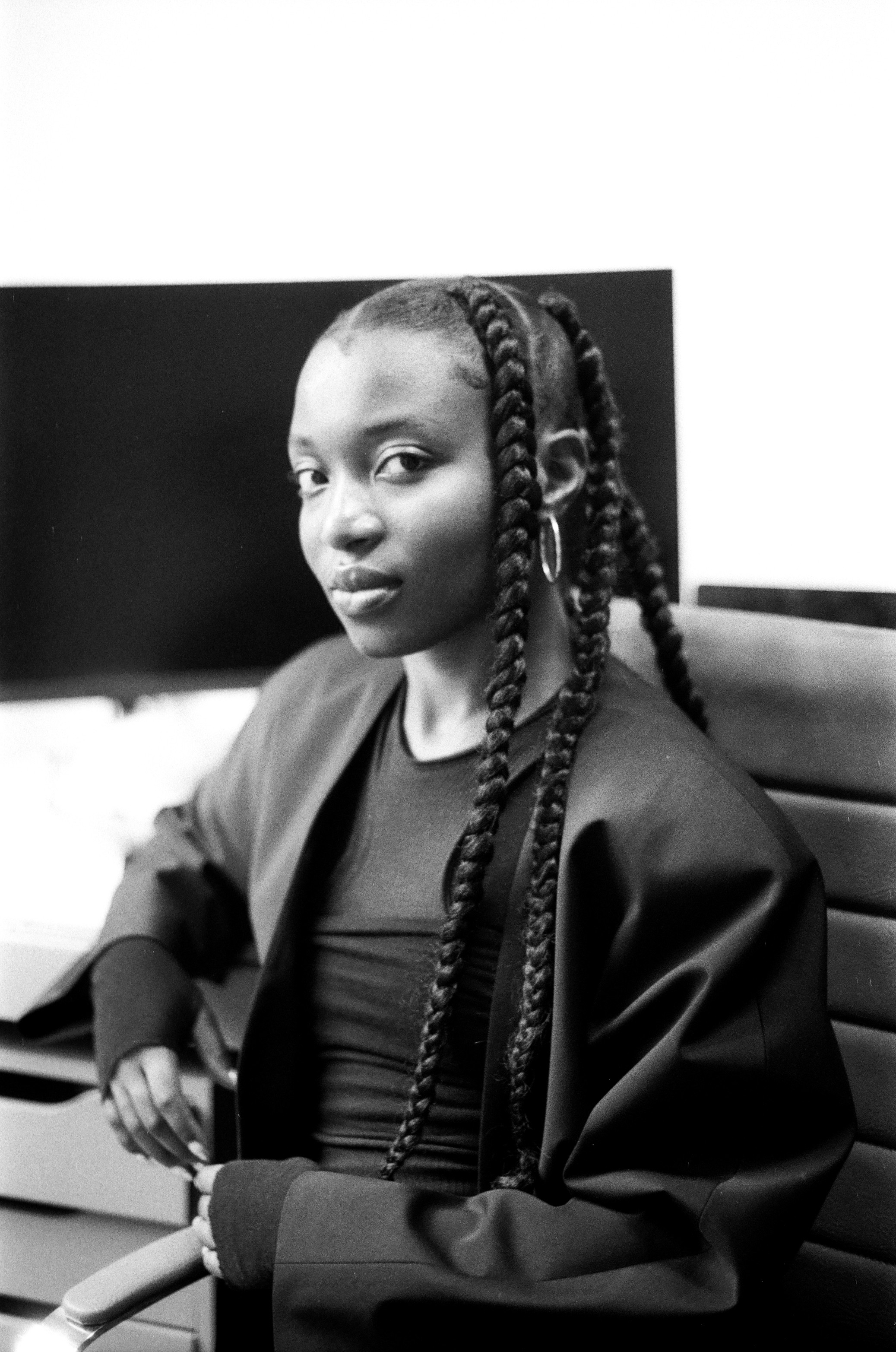 Black and white portrait of a young Black woman with long braids, wearing a dark blazer, looking at the camera.