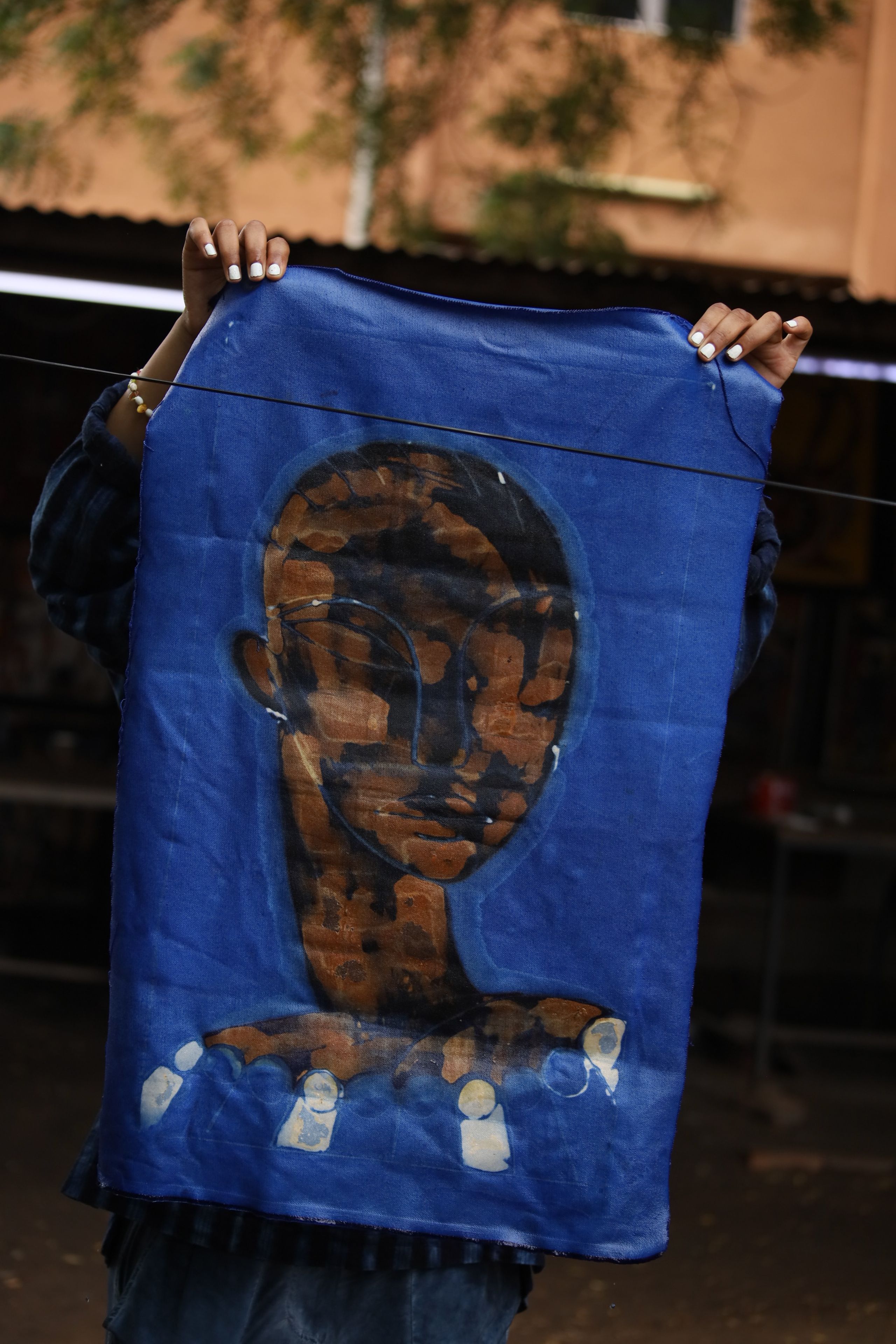 A person holding a blue fabric with a brown and black abstract head design.