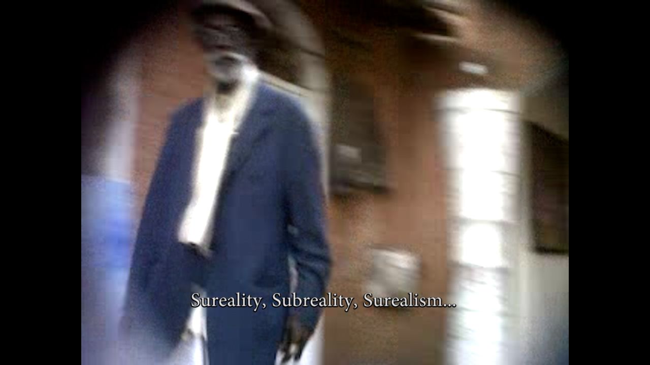 Blurred image of an older man with a white beard wearing a dark suit, with the text "Sureality, Subreality, Surrealism..." at the bottom.
