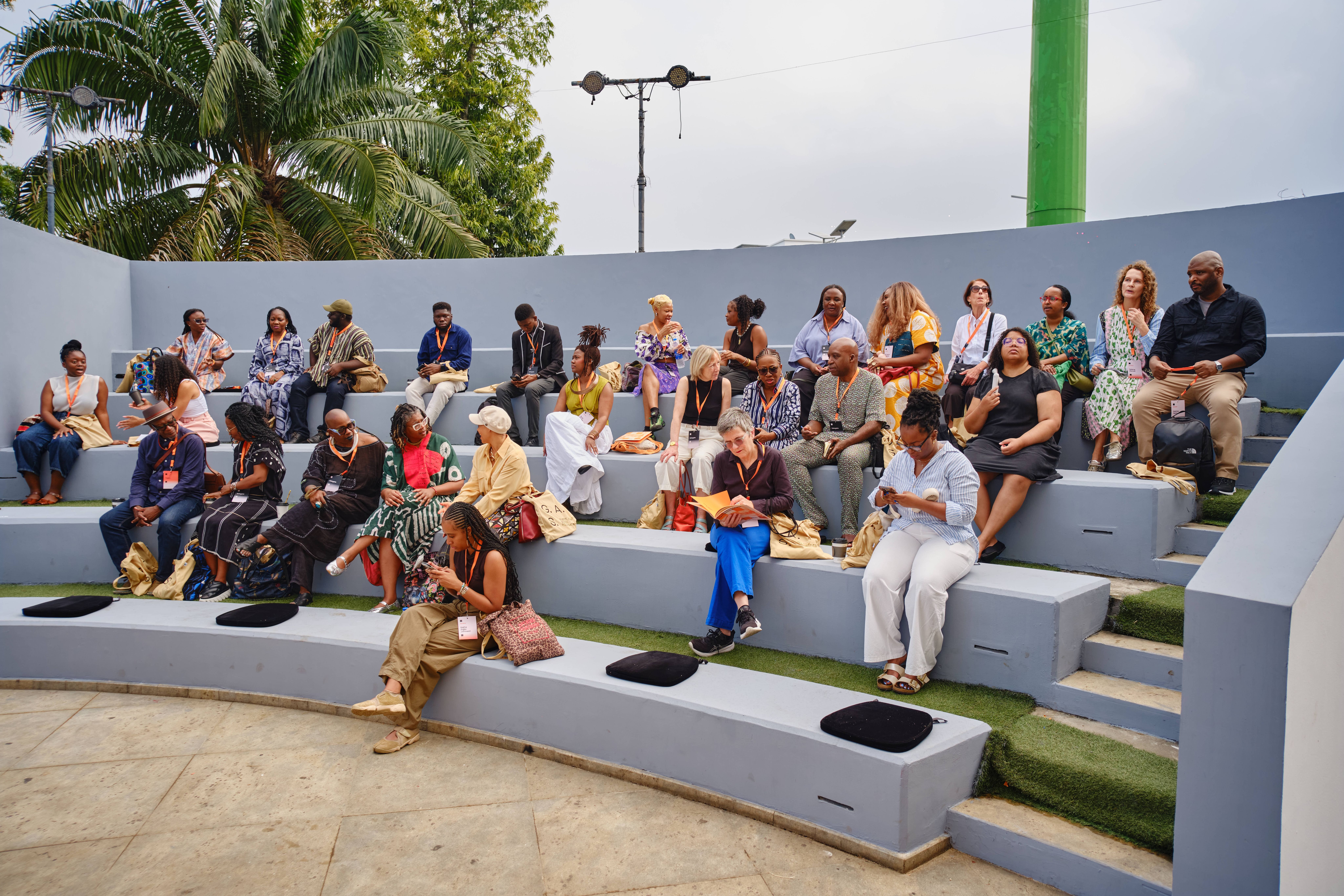 A diverse group of adults sits on outdoor tiered steps in an amphitheater-like setting.
